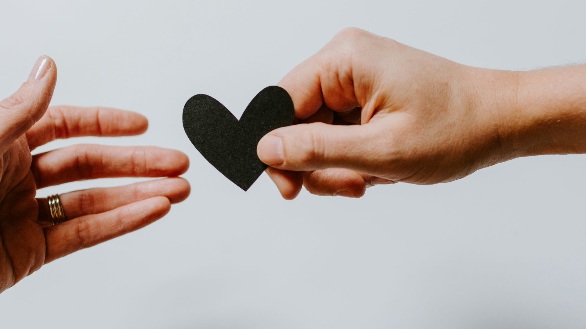 person reaching black heart cutout paper