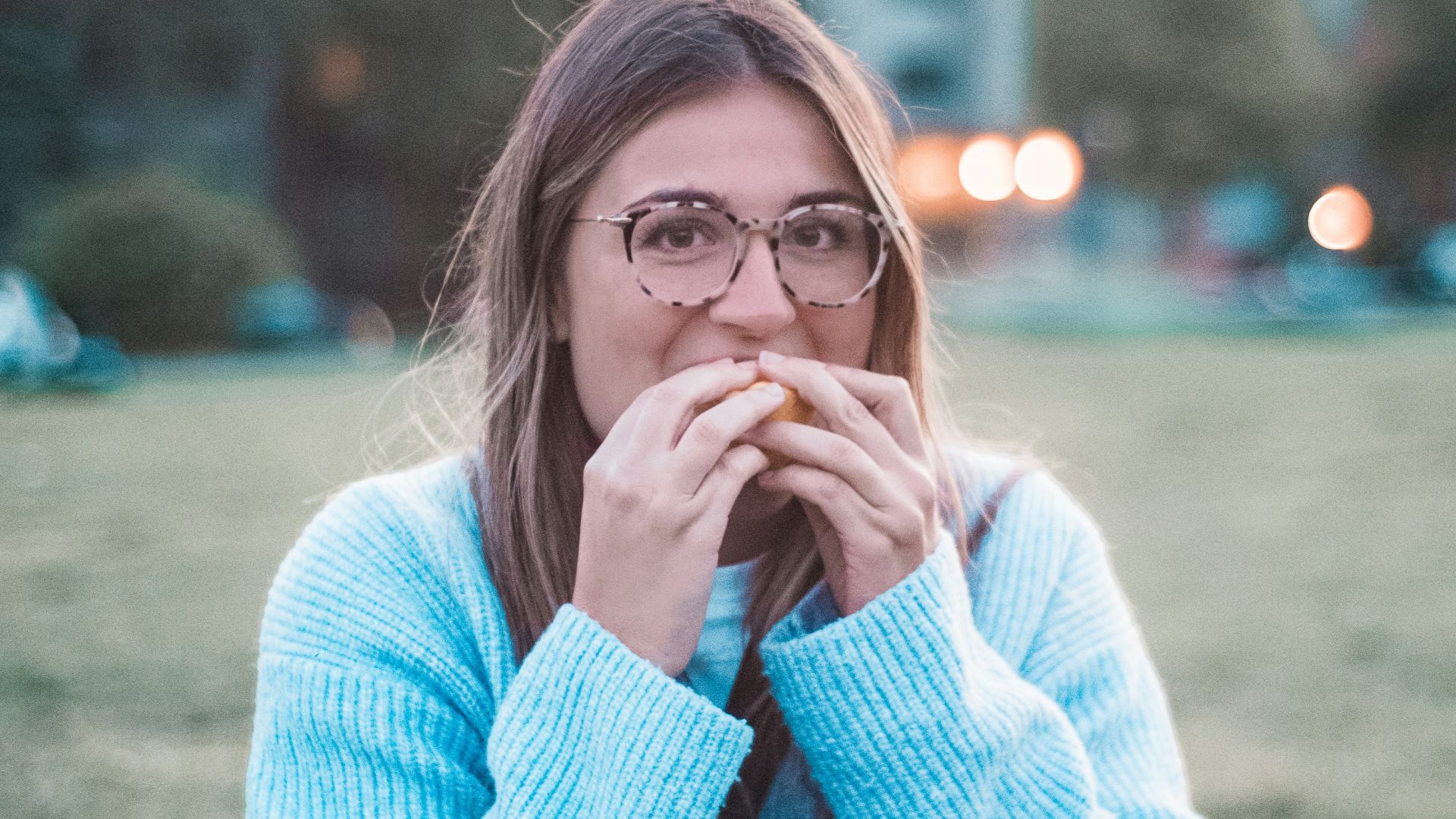 woman in blue sweater eating outdoors