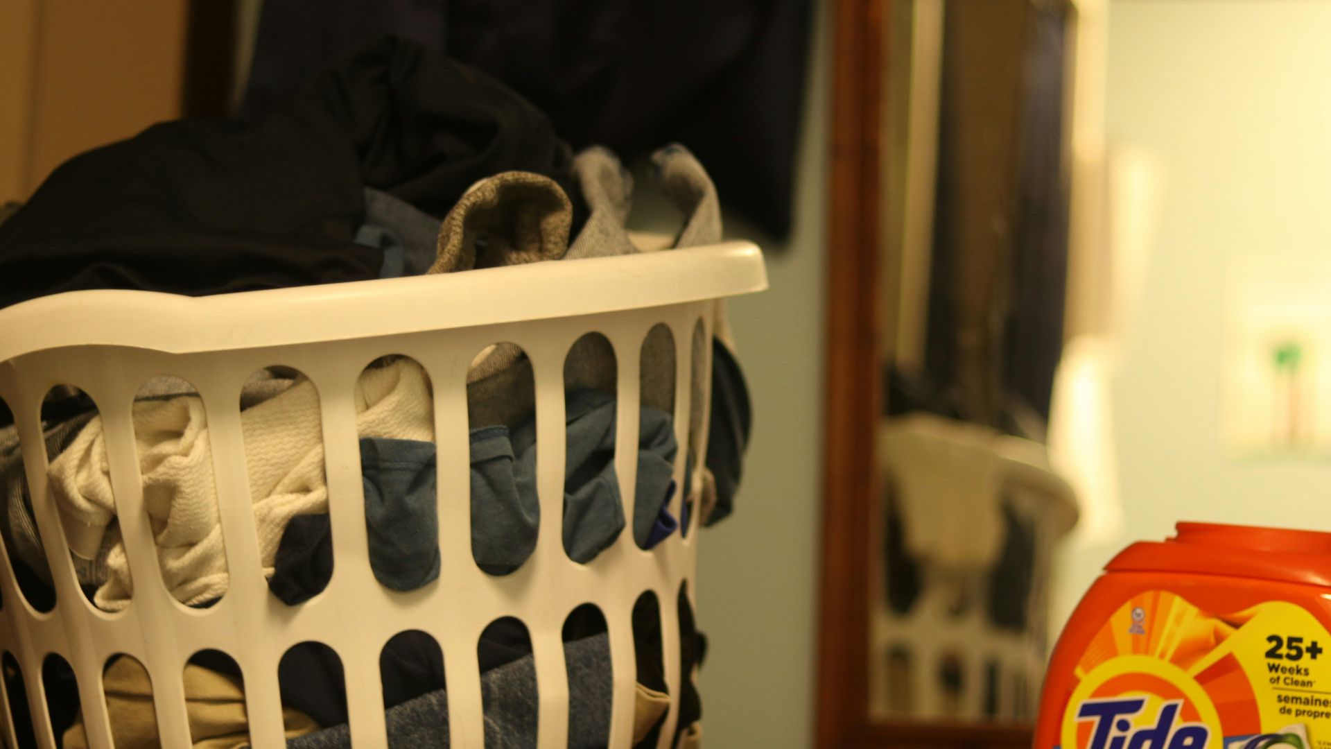 a laundry basket filled with clothes next to a bottle of tide