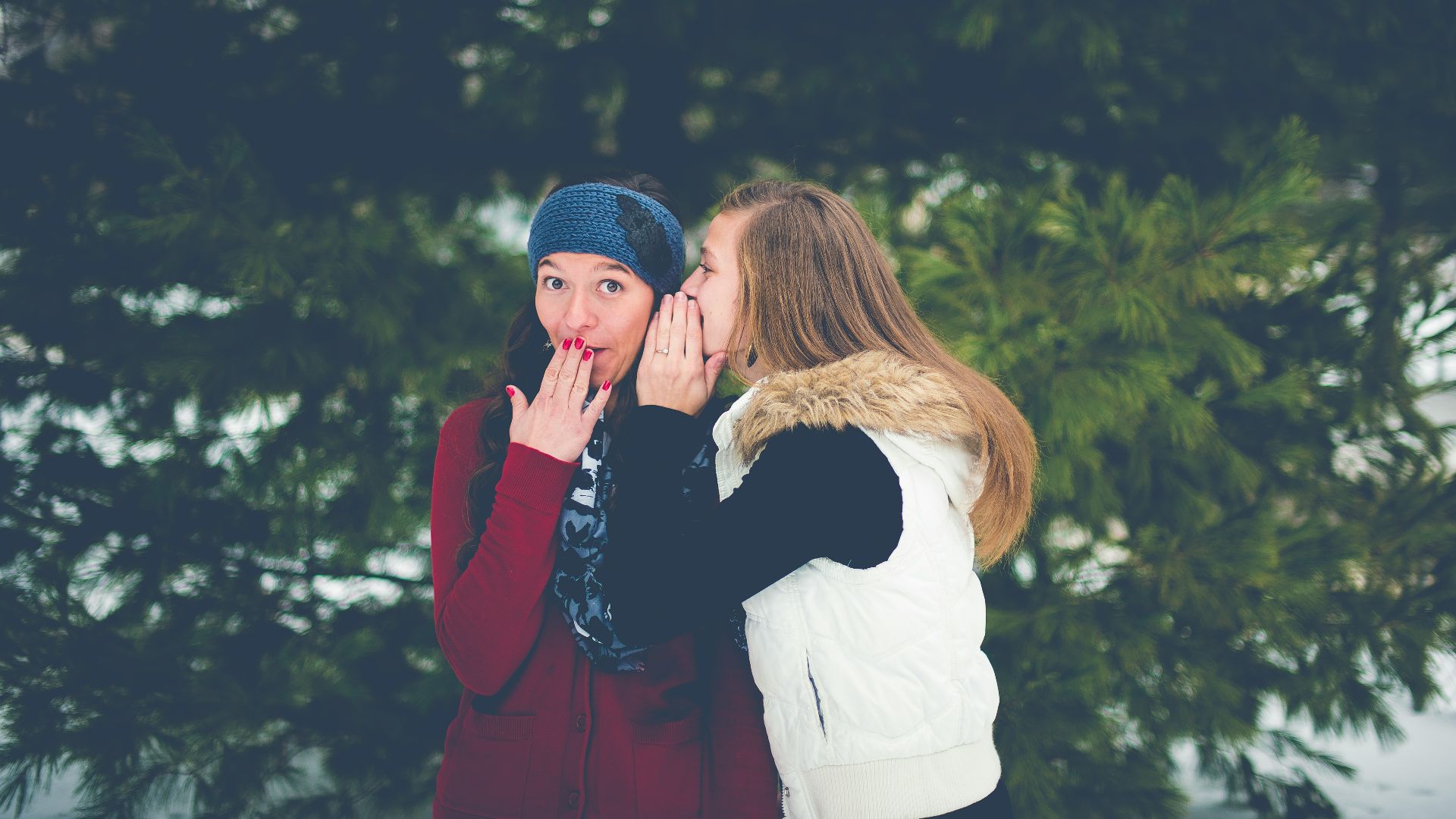 woman whispering on woman's ear while hands on lips
