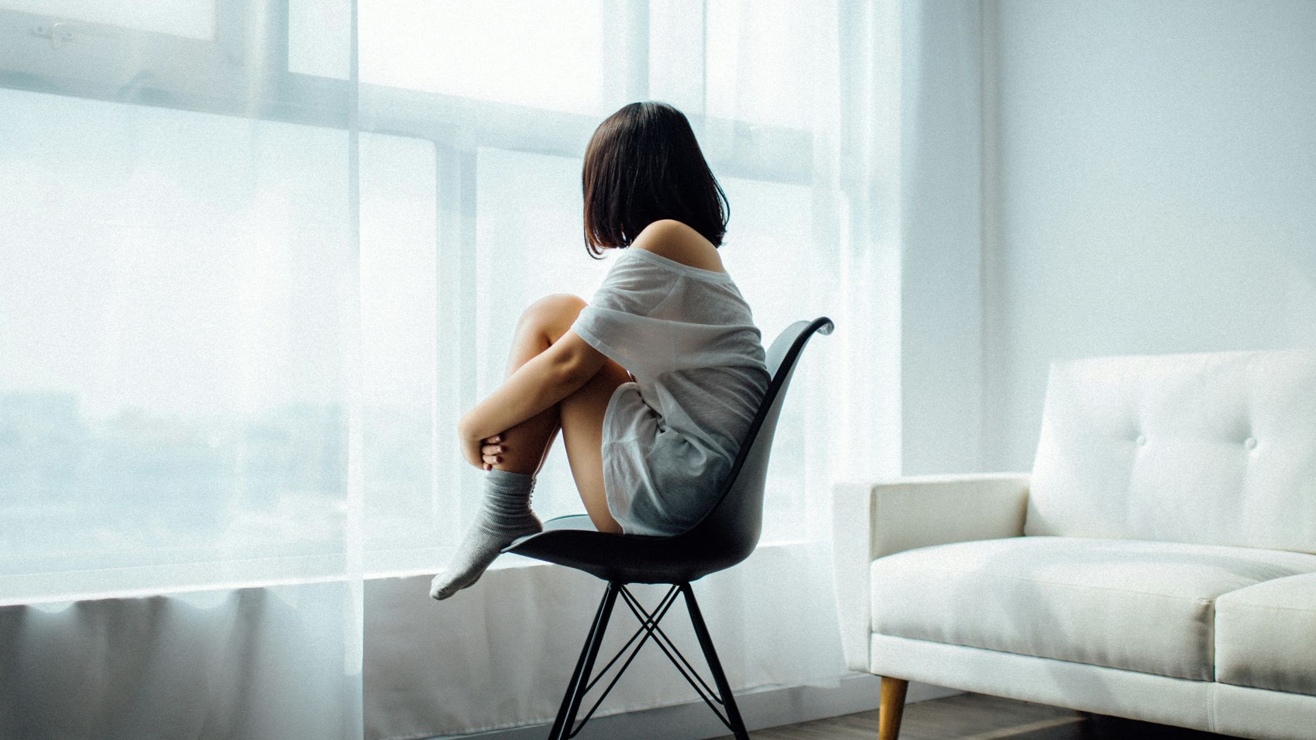 woman sitting on black chair in front of glass-panel window with white curtains