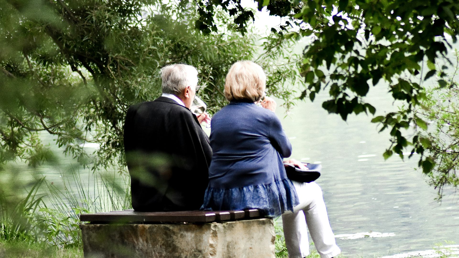 two people sitting on pavement facing on body of water