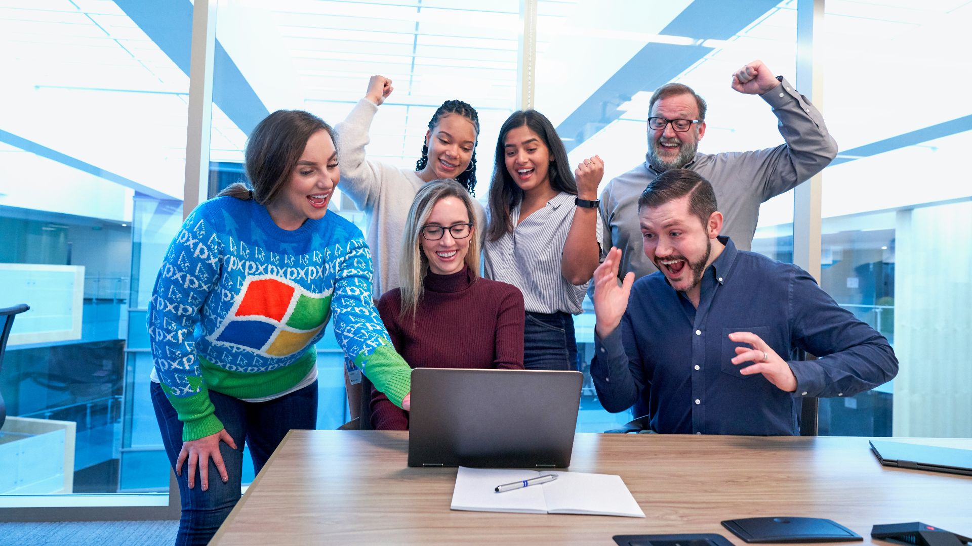 men and women sitting and standing by the table looking happy while staring at laptop