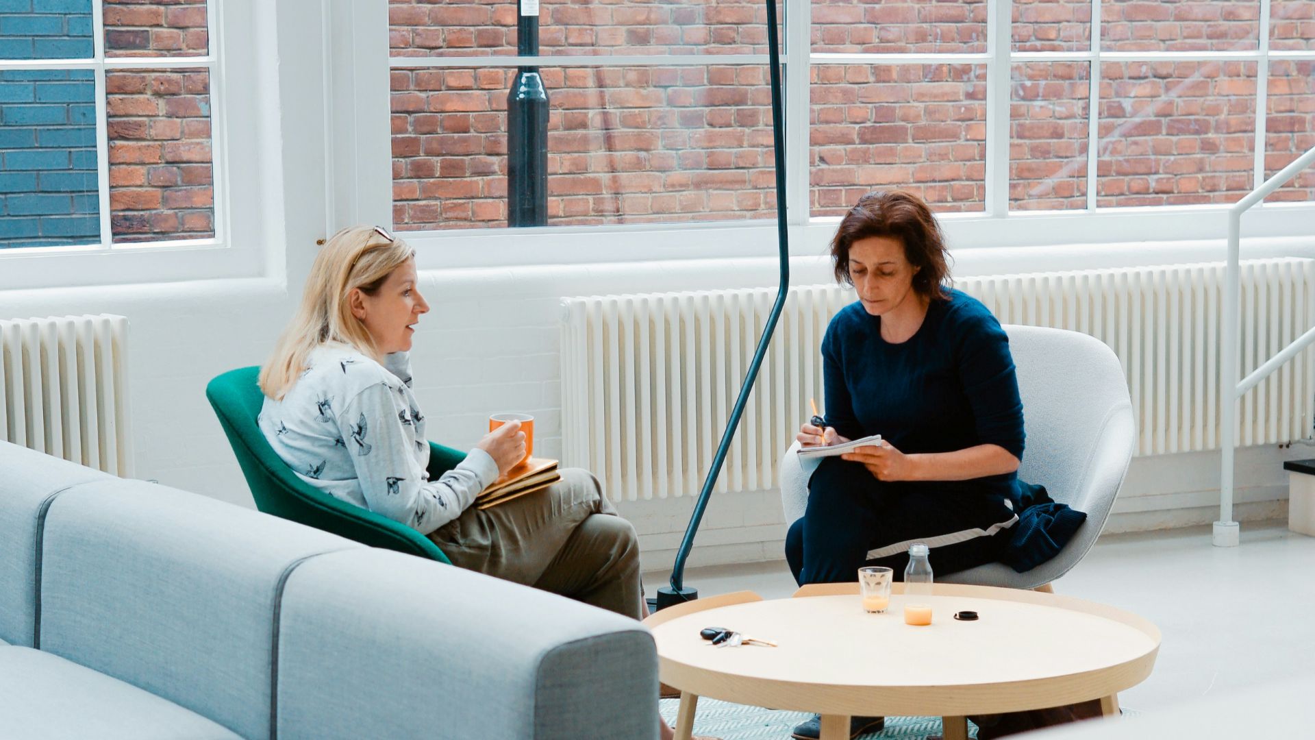 two woman sits on sofa chairs inside house