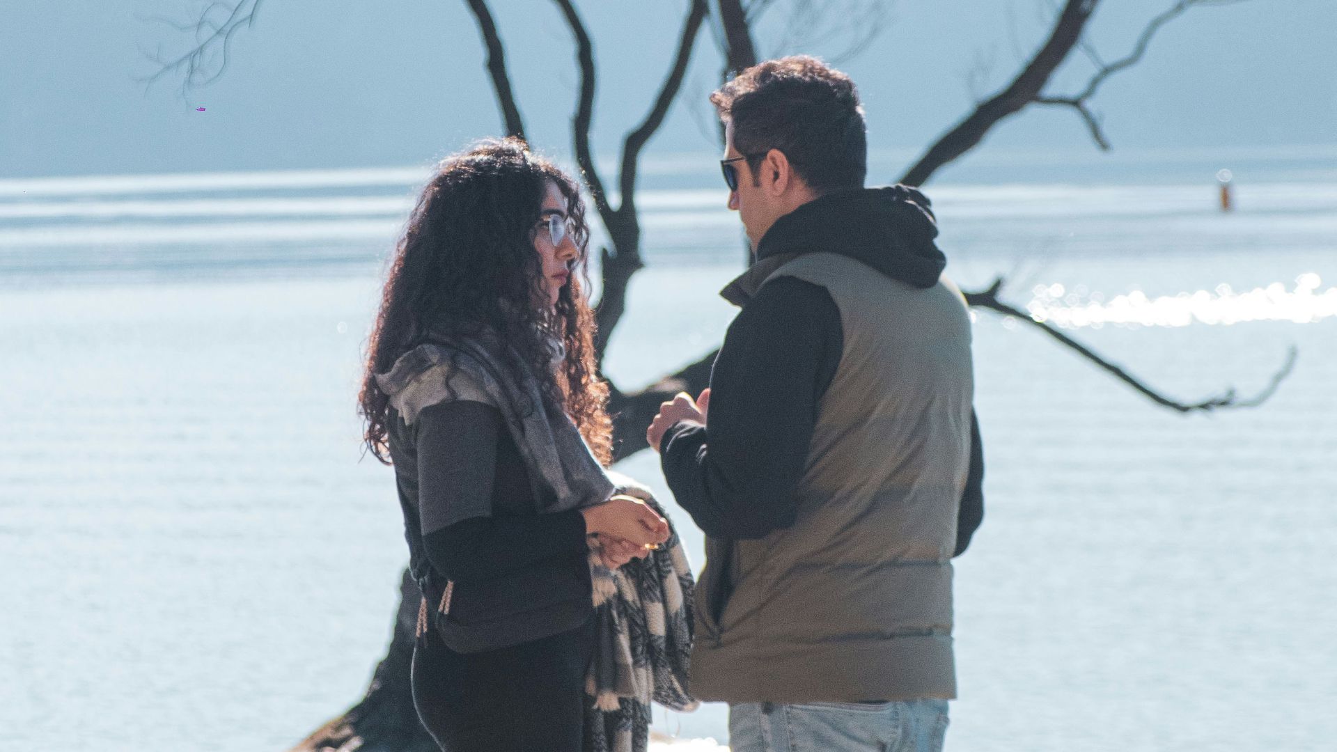 A man and woman standing on a beach next to a tree