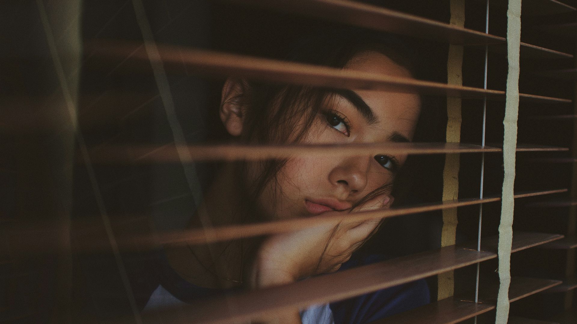a woman looking out of a window with blinds