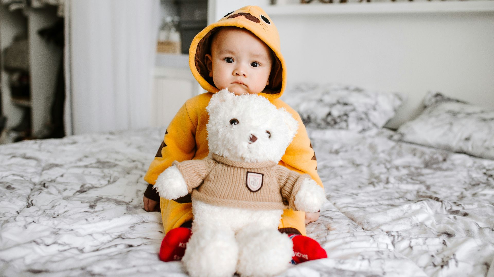 toddler sitting on bed beside white bear plush toy