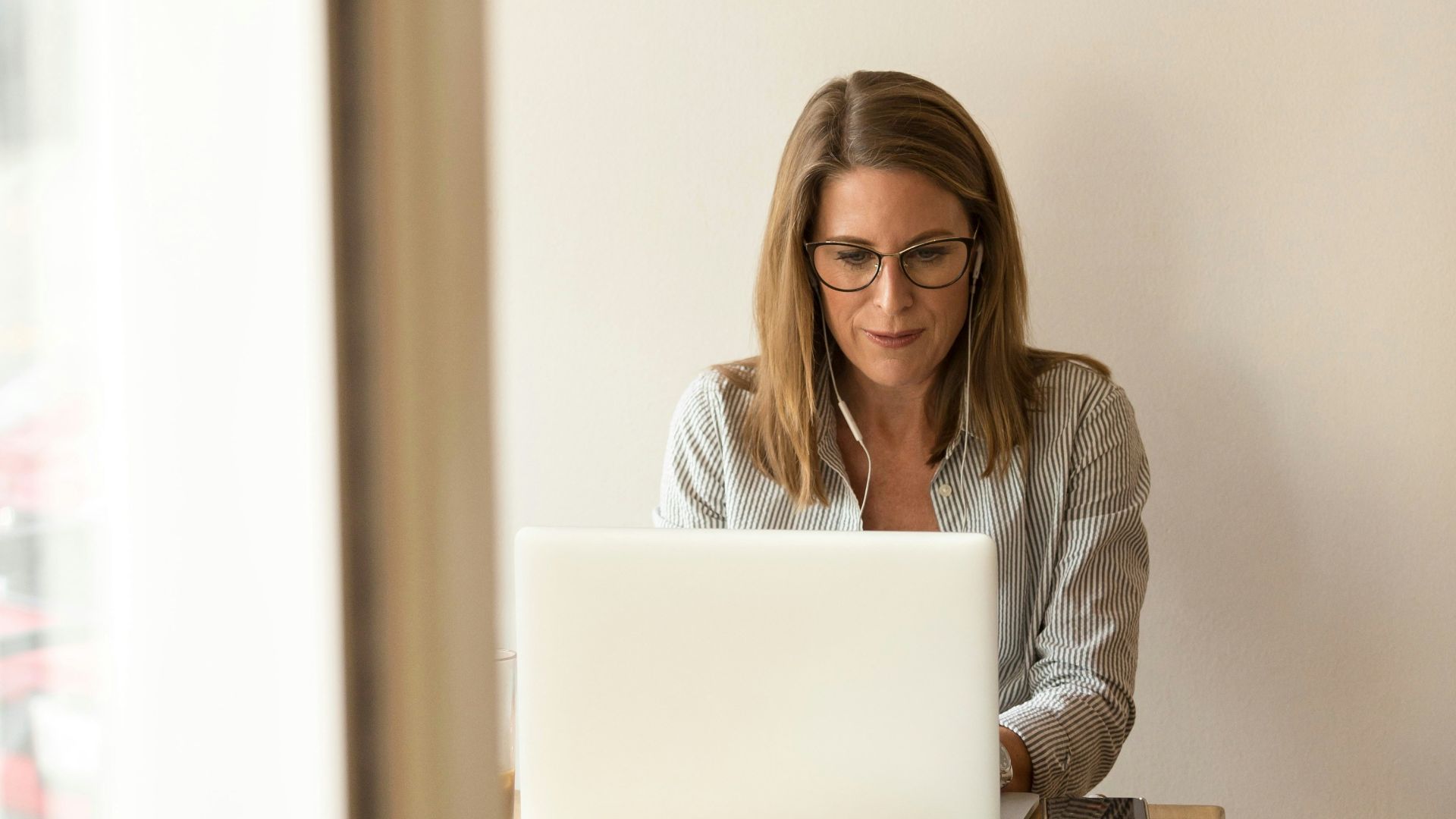 woman wearing grey striped dress shirt sitting down near brown wooden table in front of white laptop computer