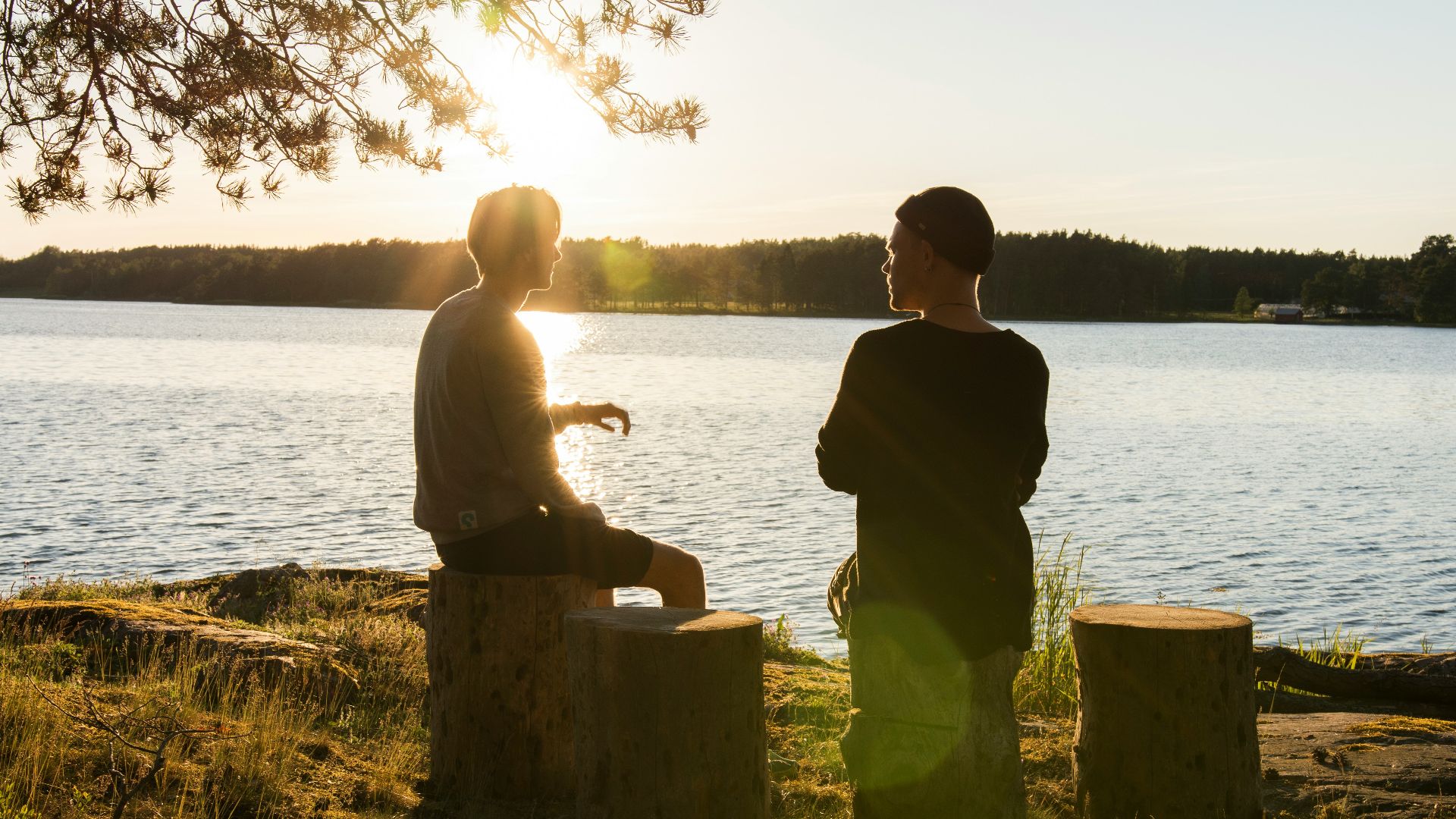 man in black jacket standing beside body of water during sunset