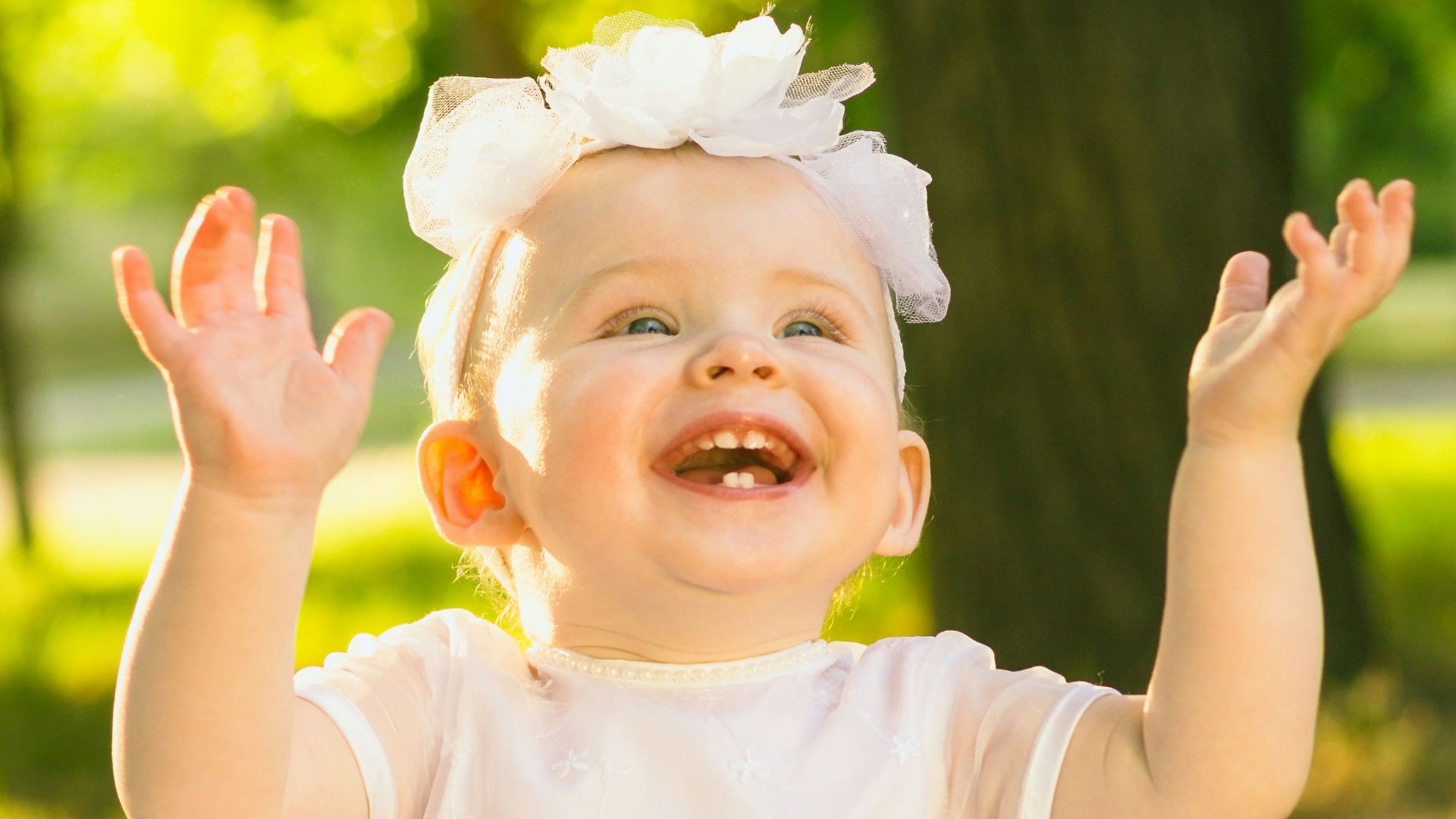 a baby girl in a white dress sitting in the grass