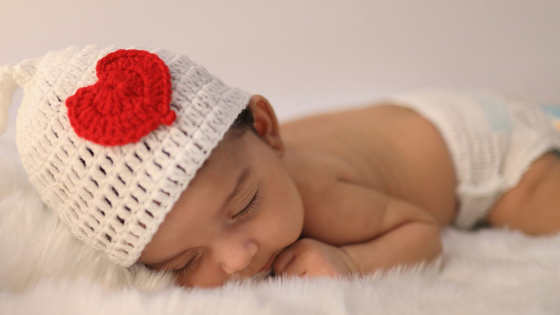 baby in white knit cap lying on white textile