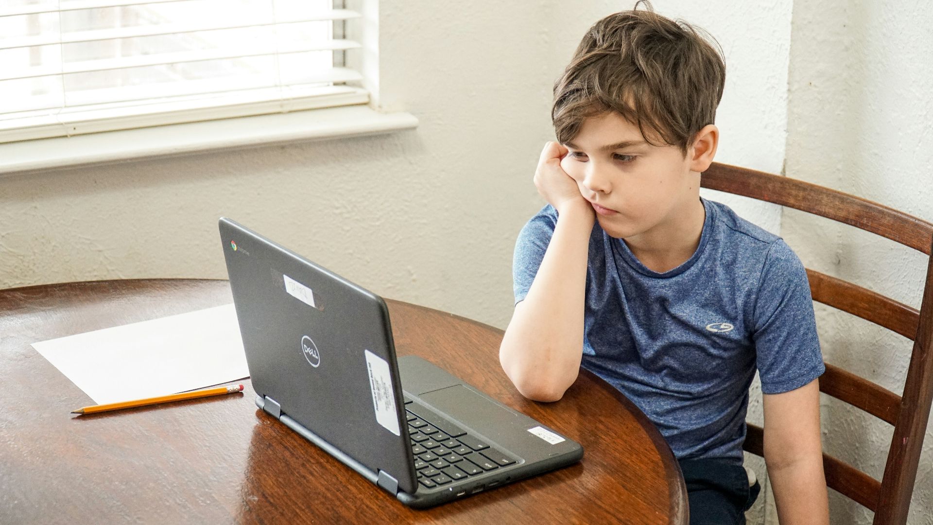 boy in blue crew neck t-shirt using macbook pro on brown wooden table