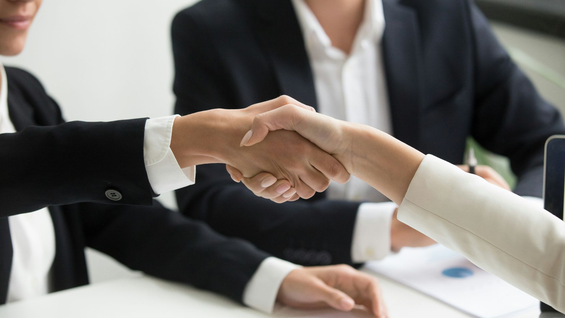 two people shaking hands in front of a laptop