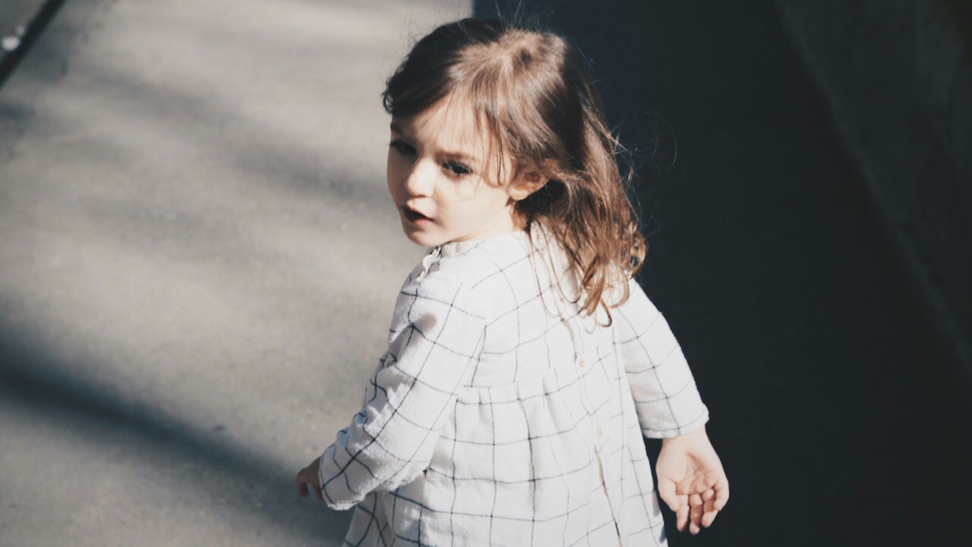 toddler girl walking on gray concrete road at daytime