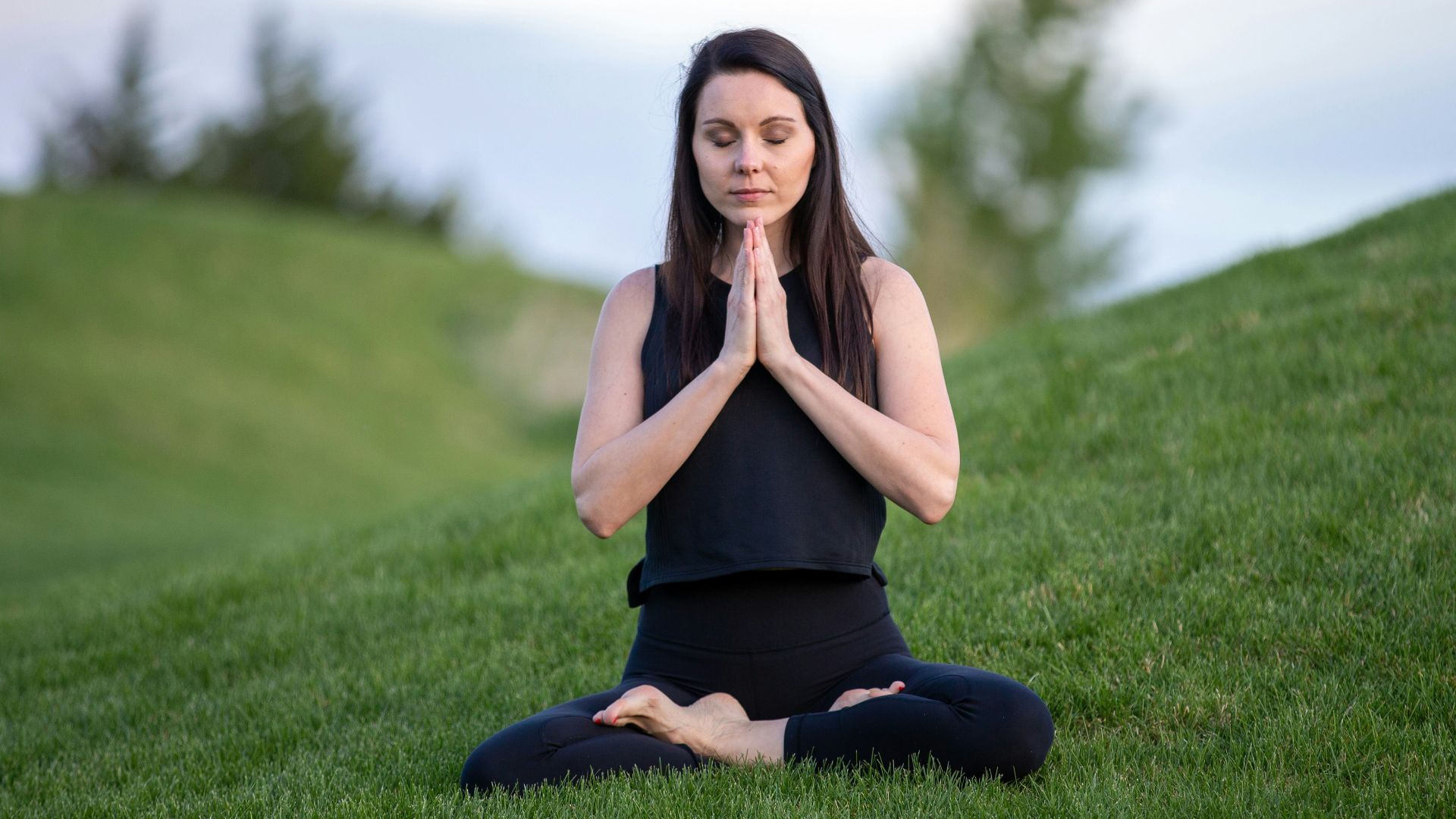woman in black tank top and black pants sitting on green grass field during daytime