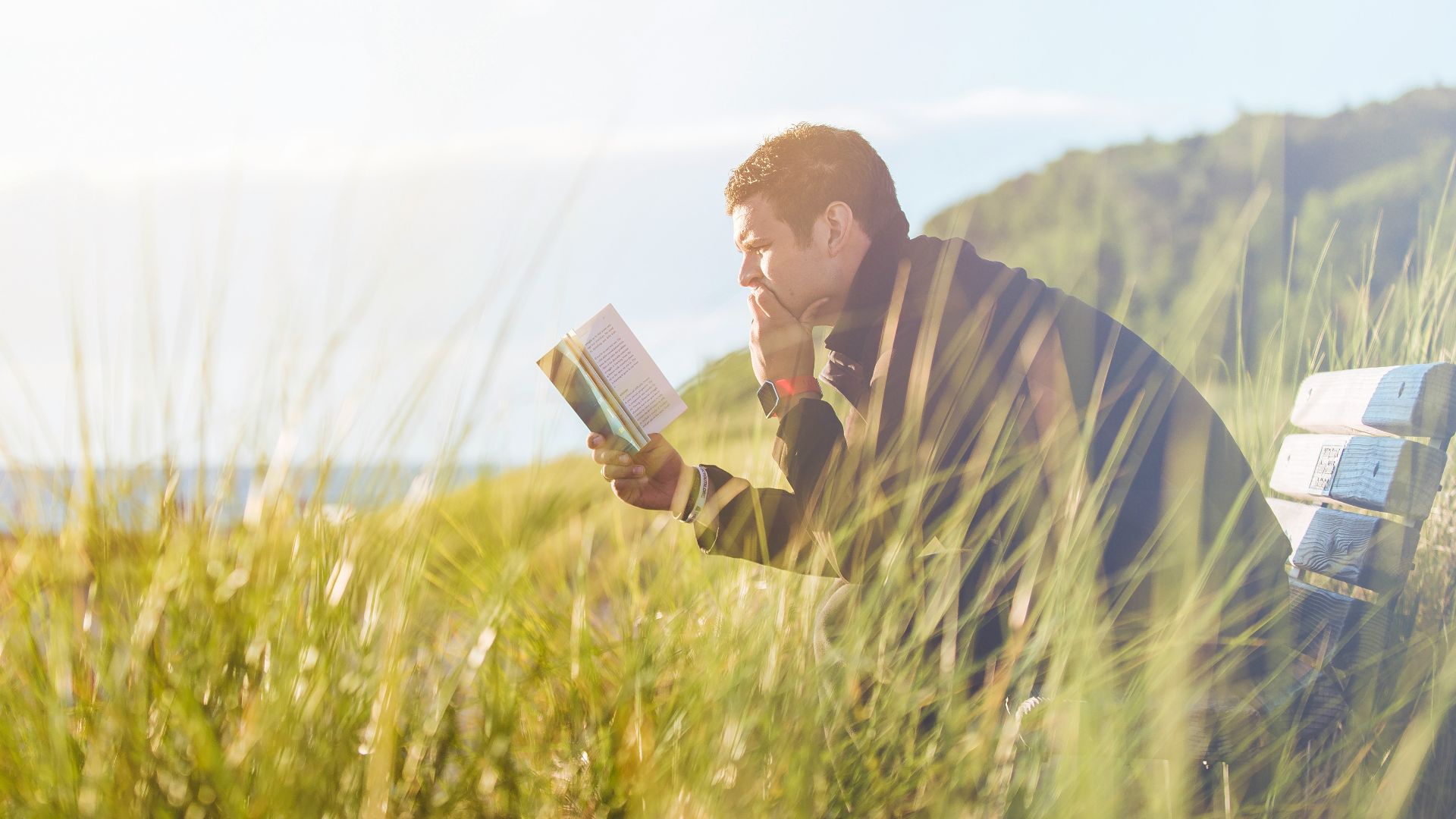 man reading book on beach near lake during daytime