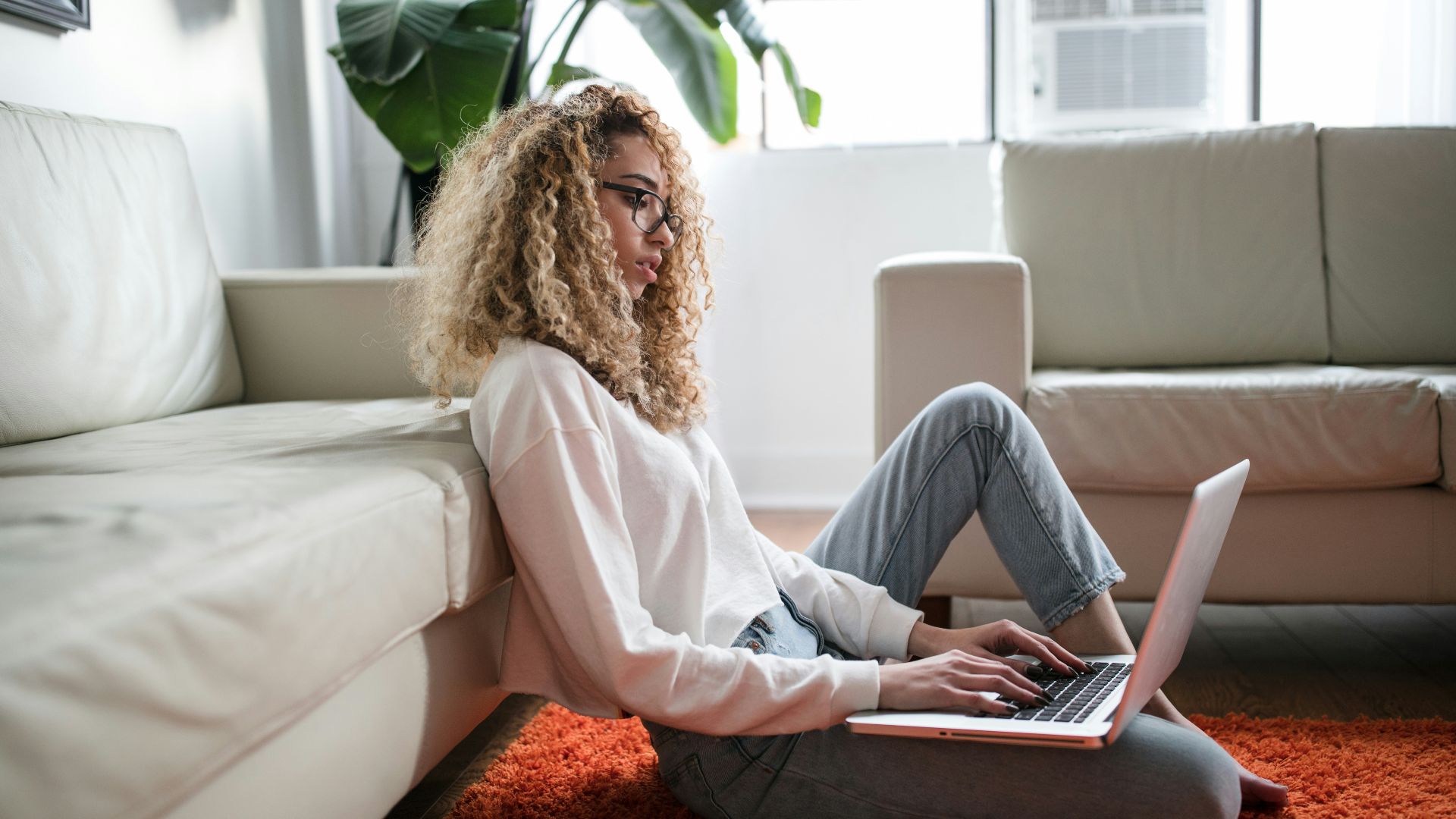 woman sitting on floor and leaning on couch using laptop