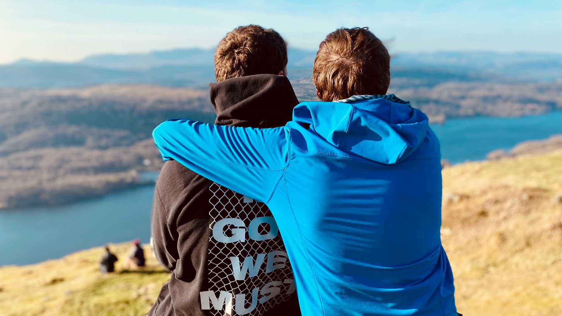 two people sitting on a hill overlooking a lake