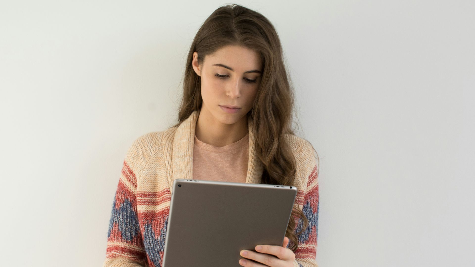 woman in beige, gray, and red sweater holding silver tablet computer
