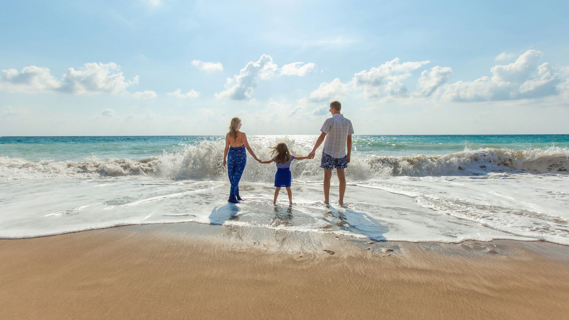 man, woman and child holding hands on seashore