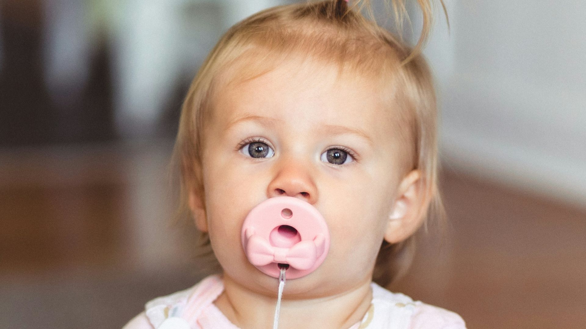 a little girl sitting on the floor with a pacifier in her mouth