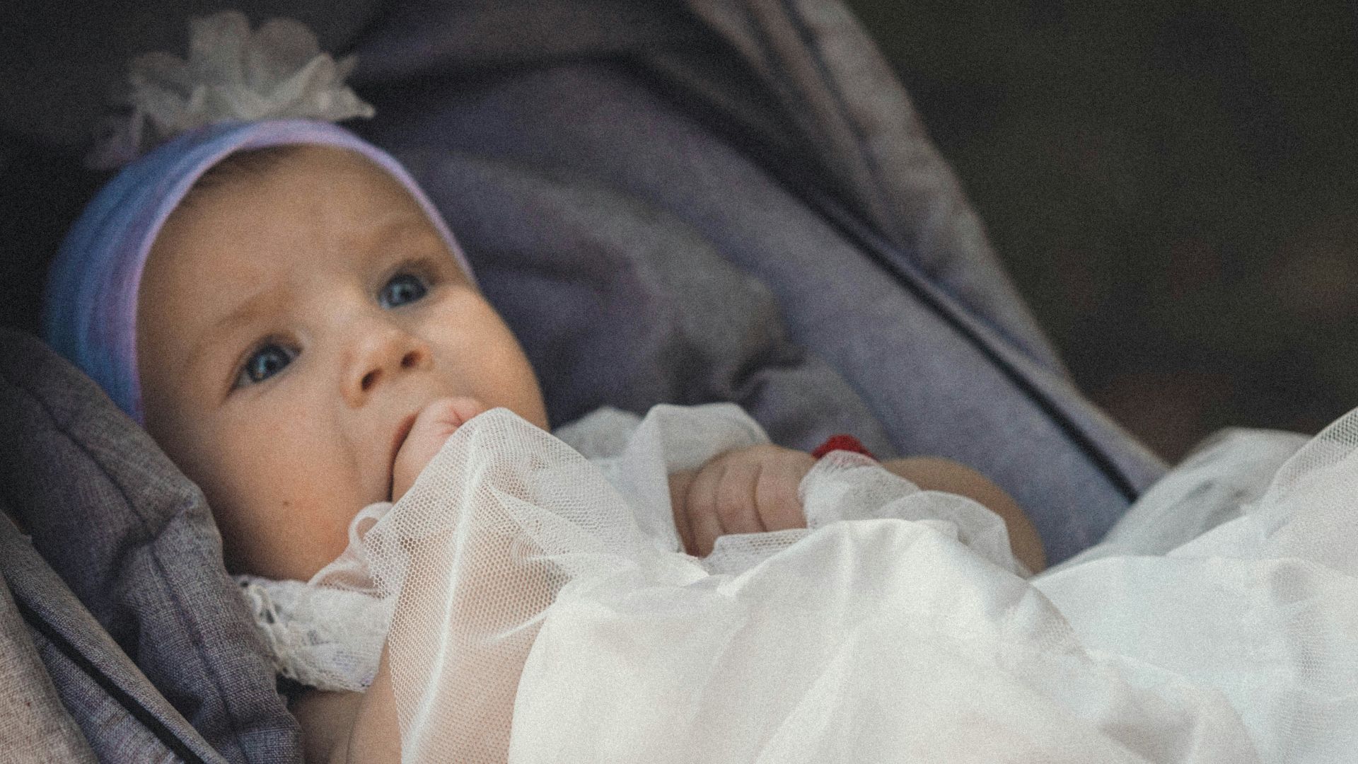 a baby in a stroller wearing a white dress