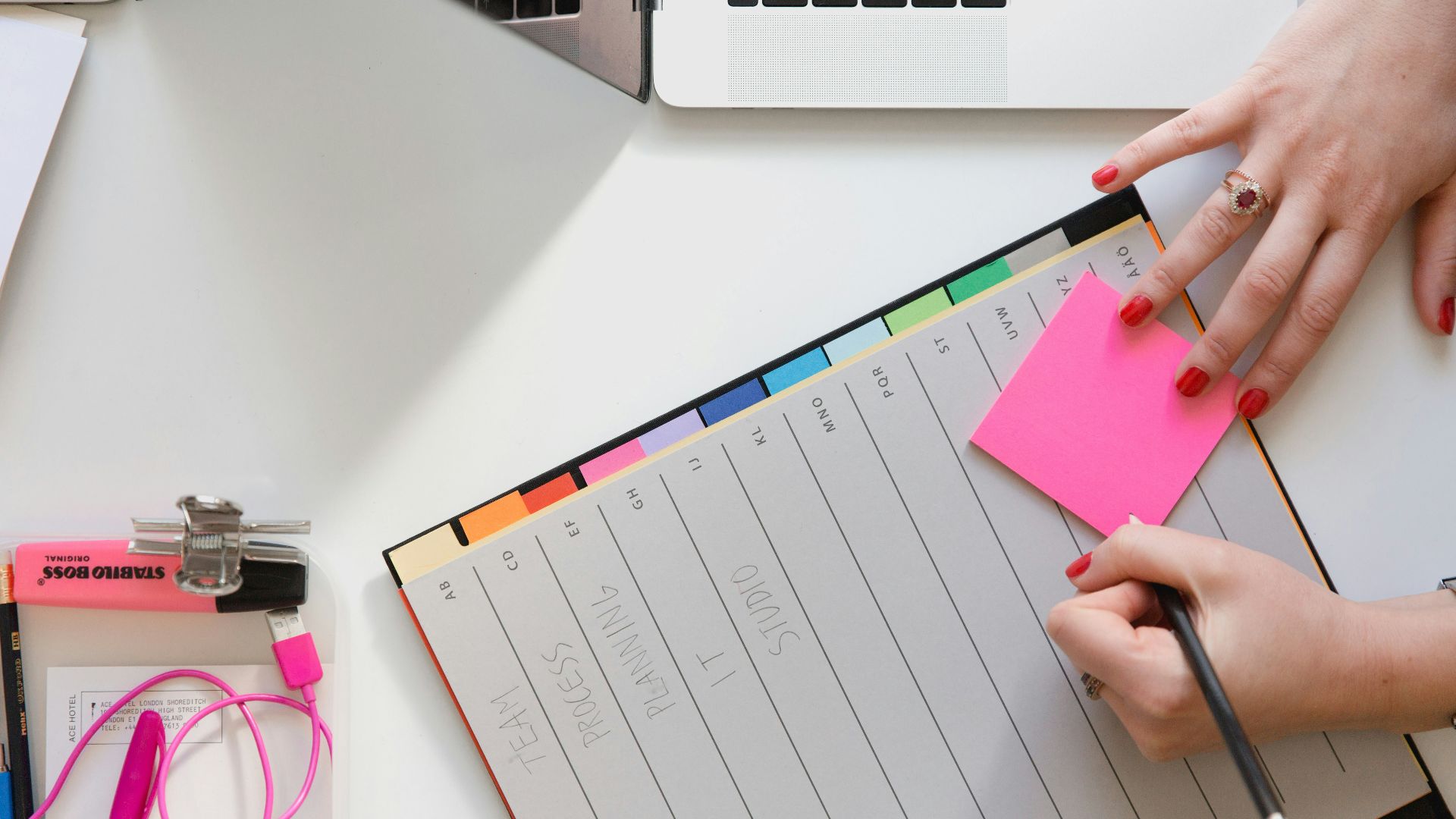 person holding pencil and stick note beside table