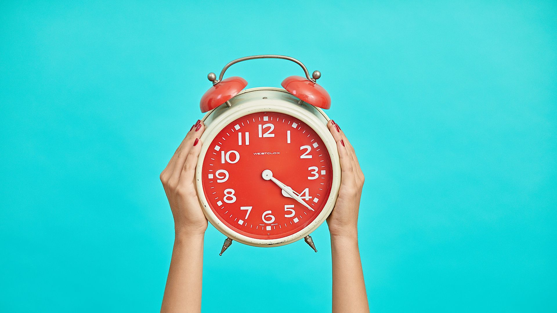 person holding red and beige twin bell analog alarm clock