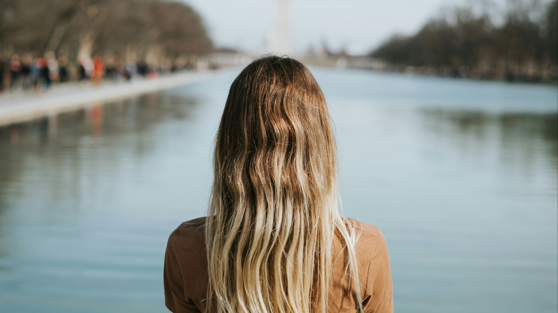 woman in brown long sleeve shirt standing near body of water during daytime