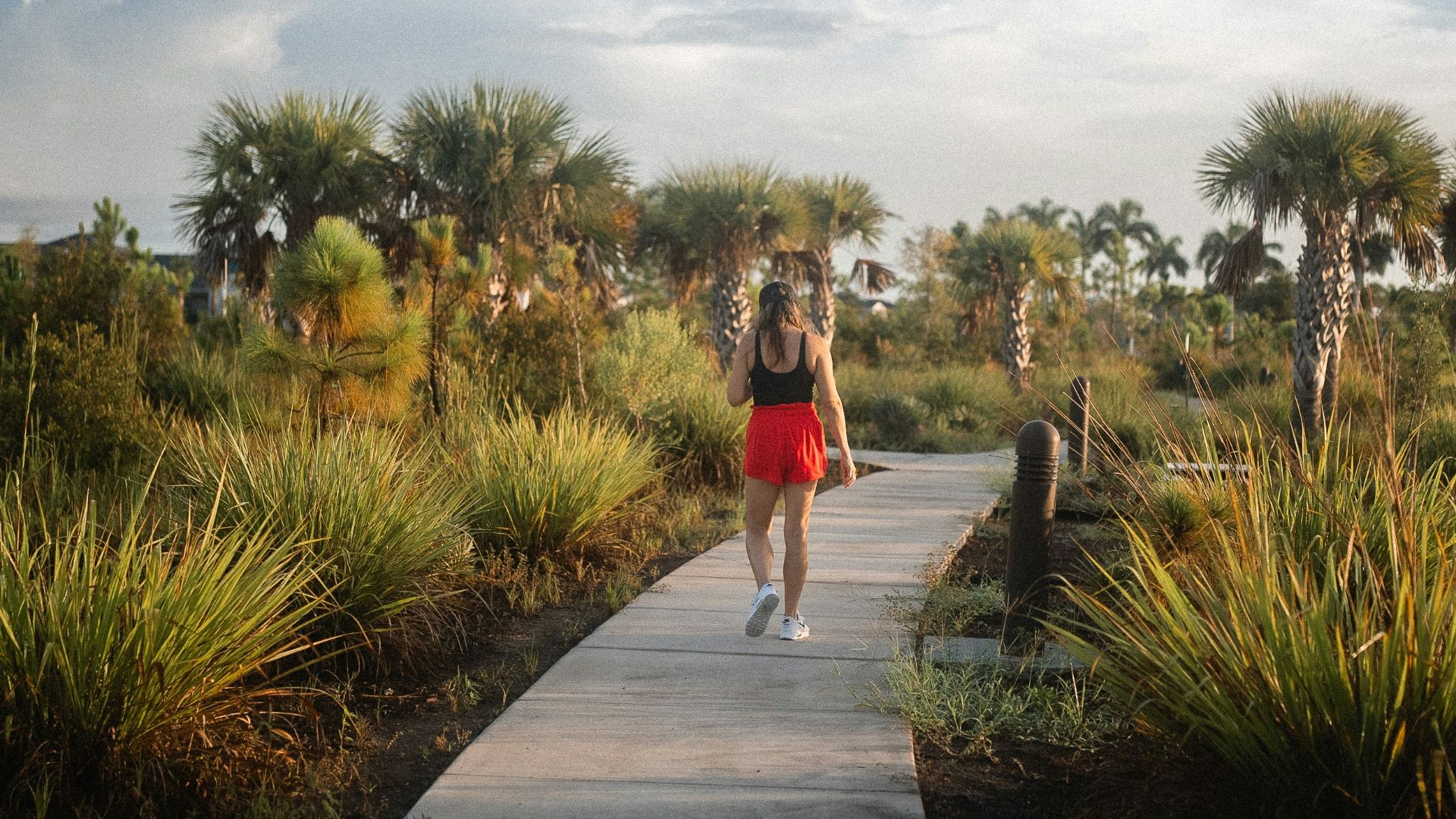 a woman walking down a path through a lush green field