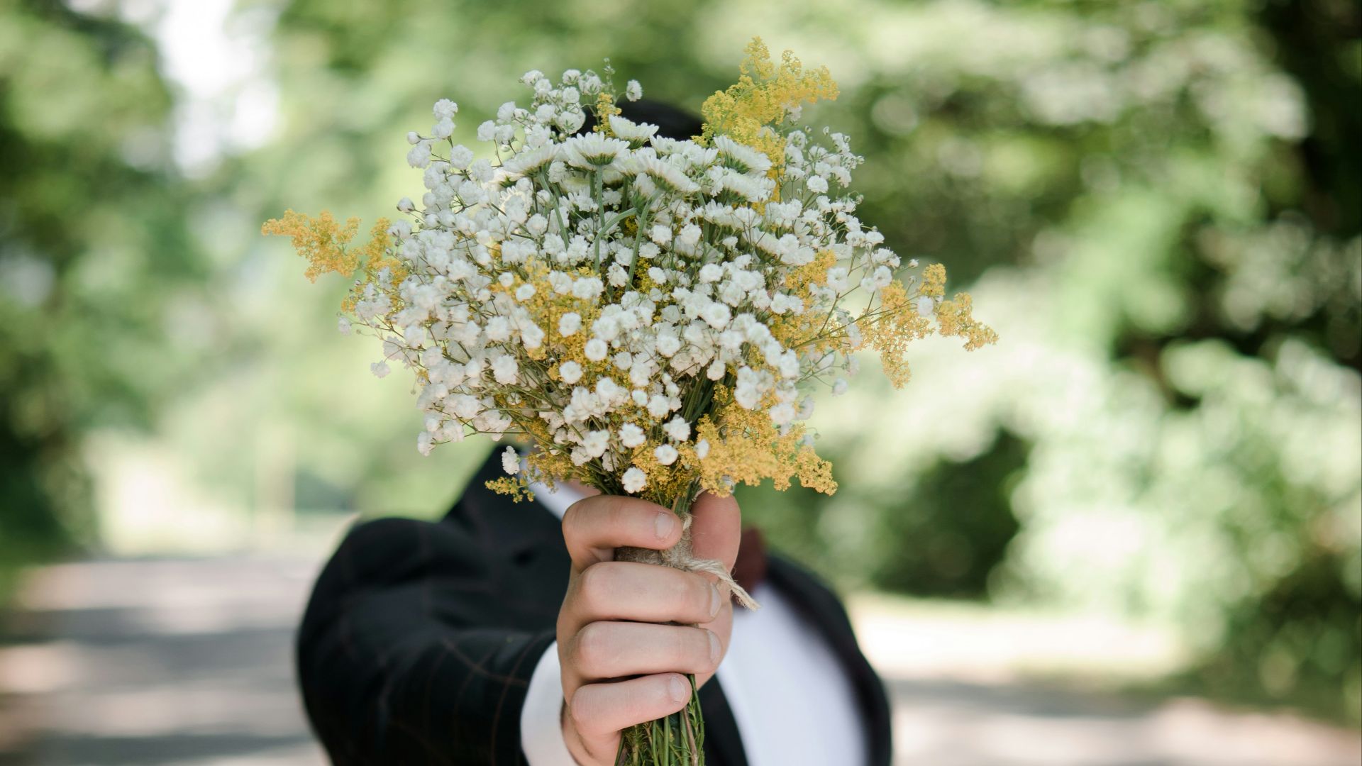 selective focus photo of man wearing black suit jacket holding flower bouquet