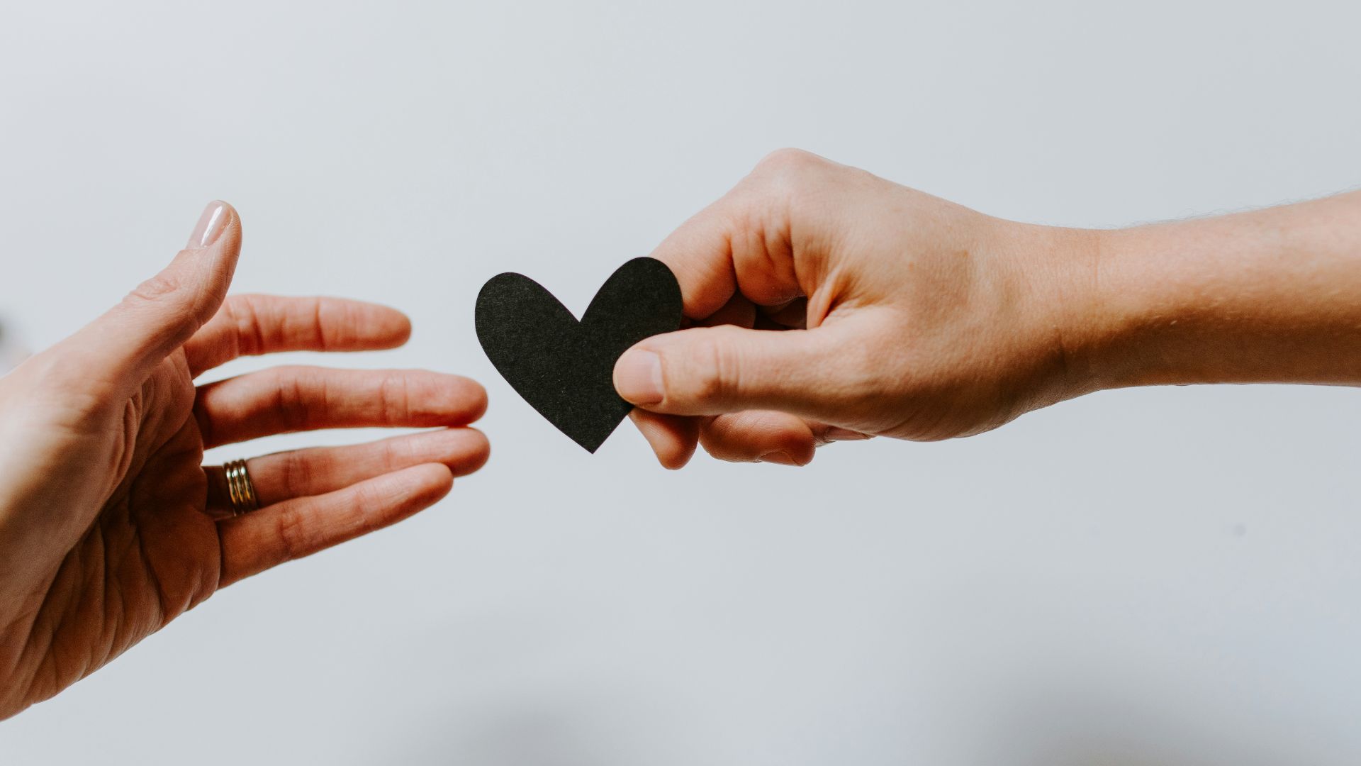 person reaching black heart cutout paper