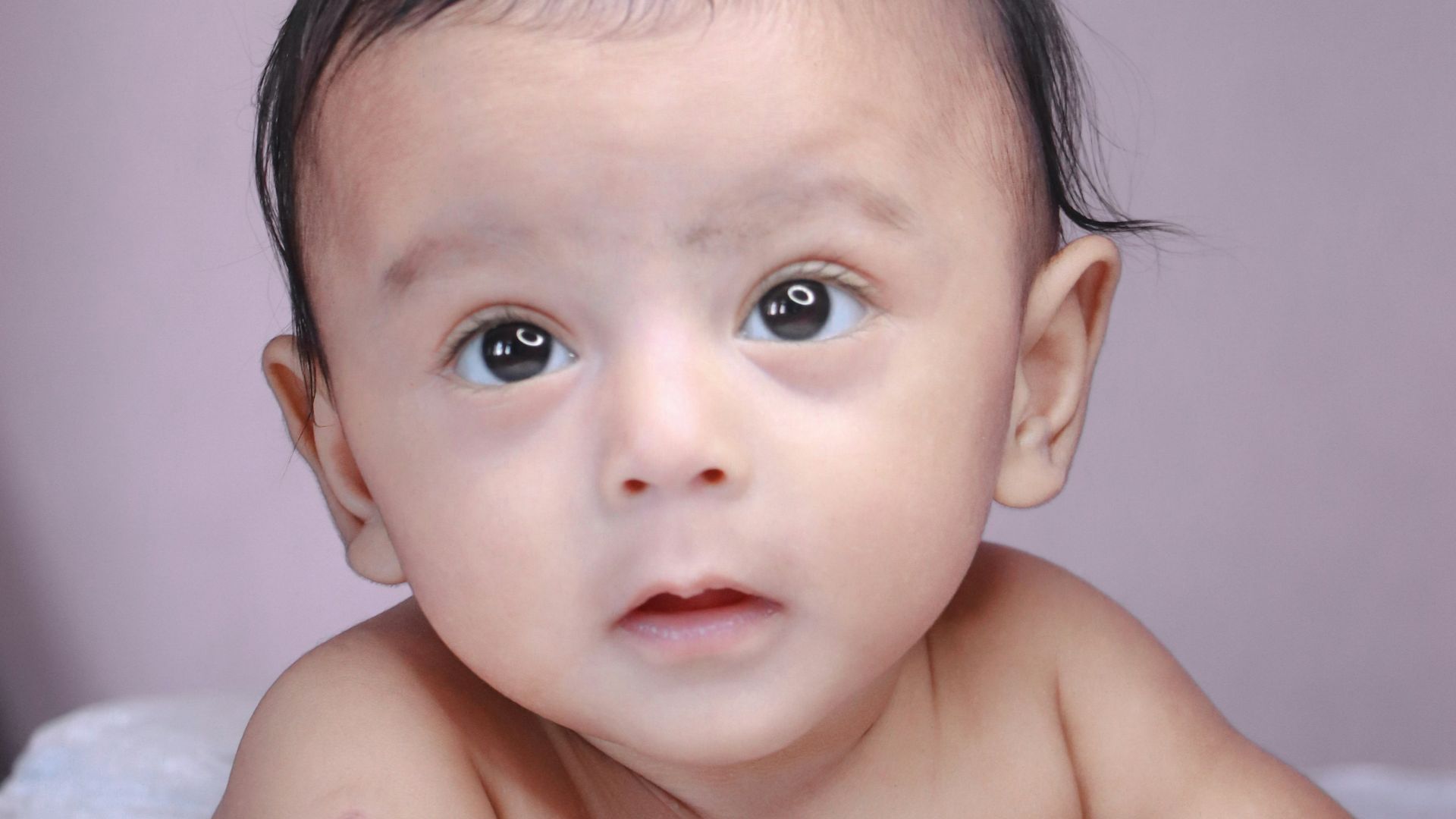 topless baby lying on white textile