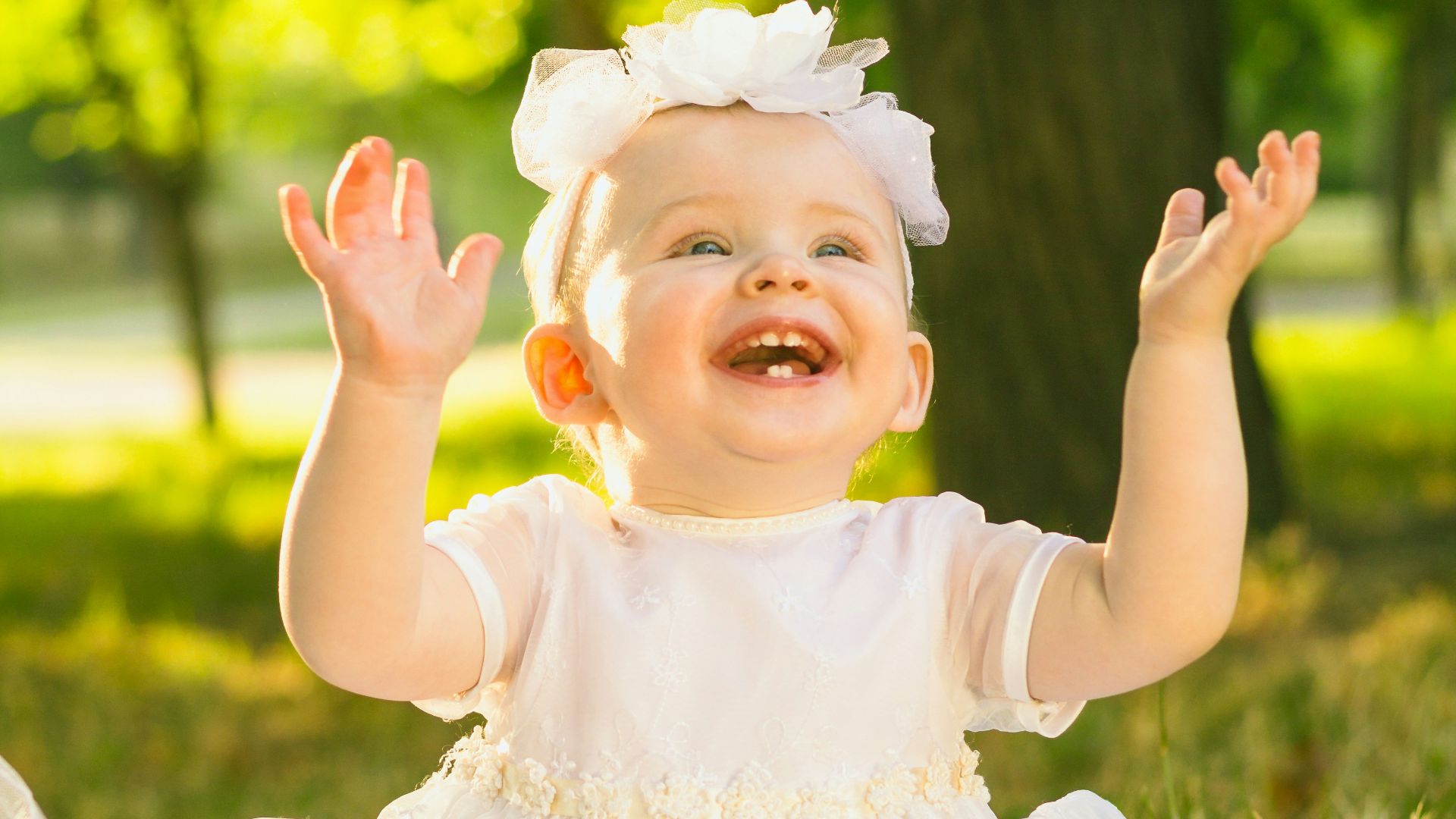 a baby girl in a white dress sitting in the grass