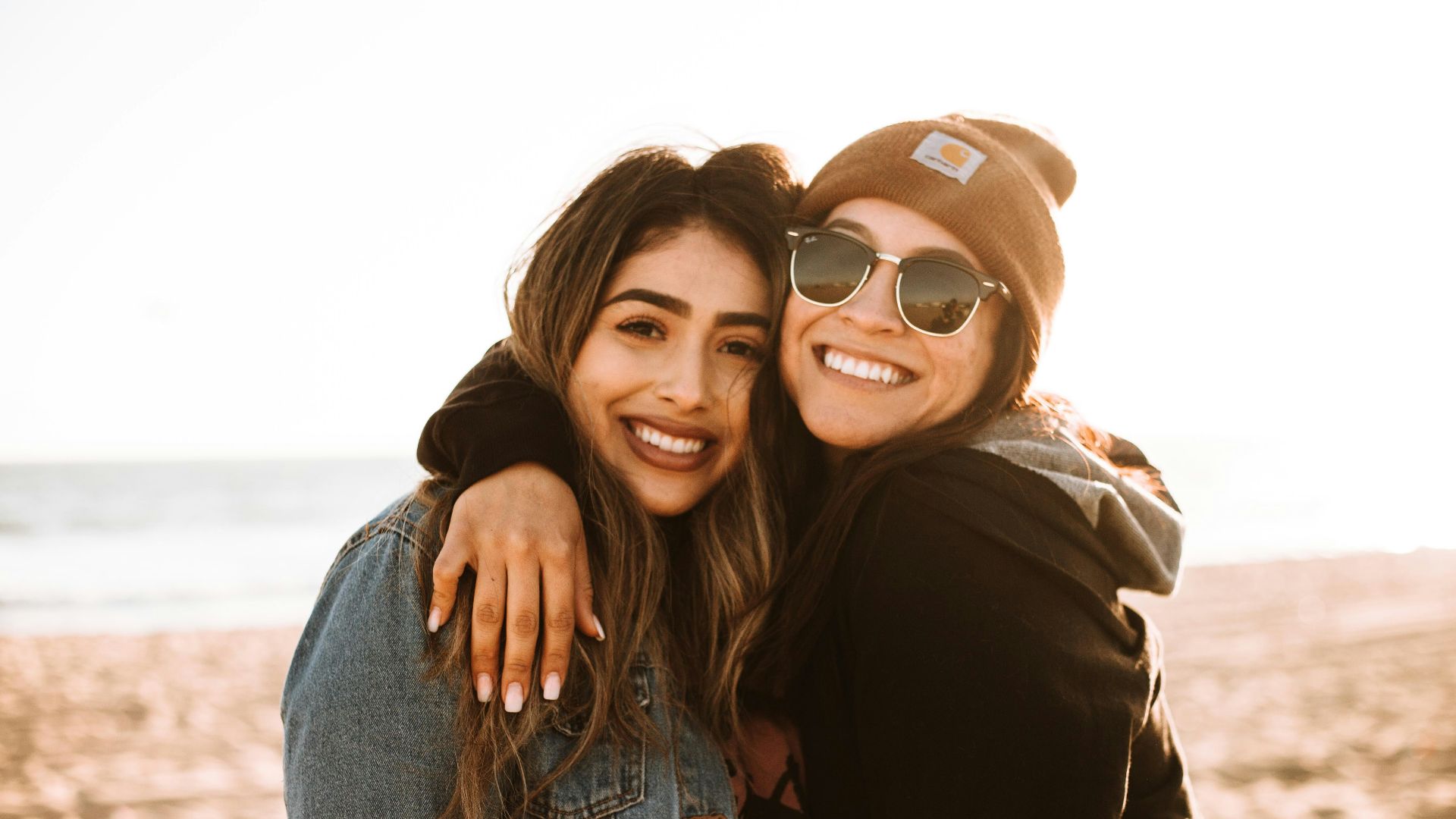 woman hugging other woman while smiling at beach