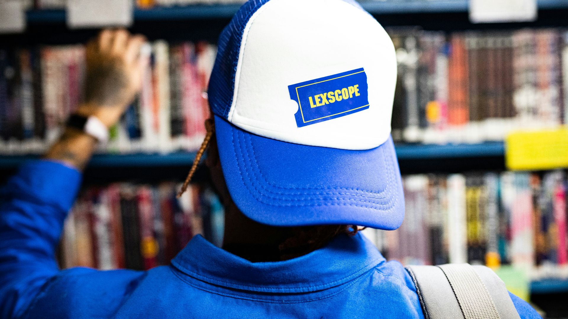 a man wearing a blue and white hat in front of a bookshelf