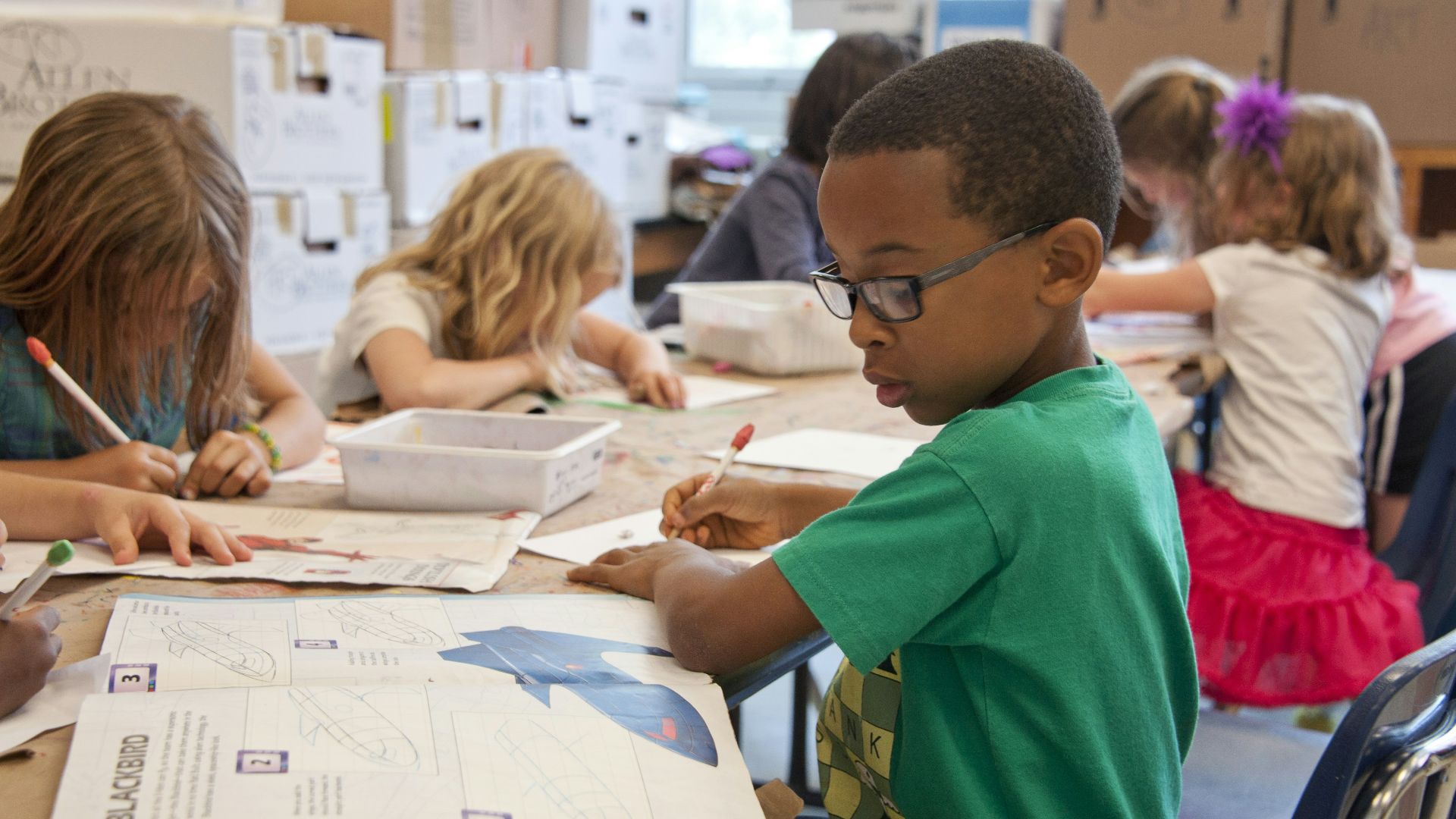 boy in green sweater writing on white paper