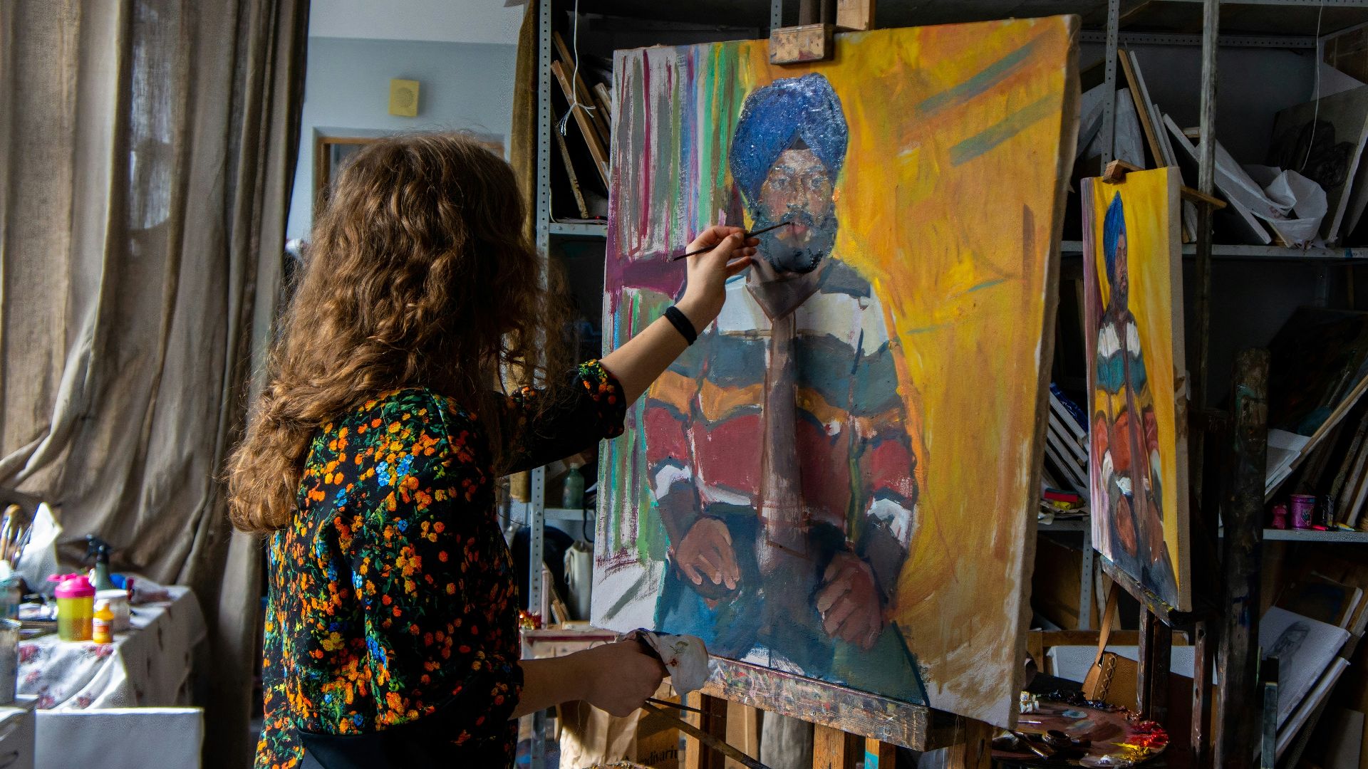 woman in black and brown floral long sleeve shirt holding painting of man in blue denim