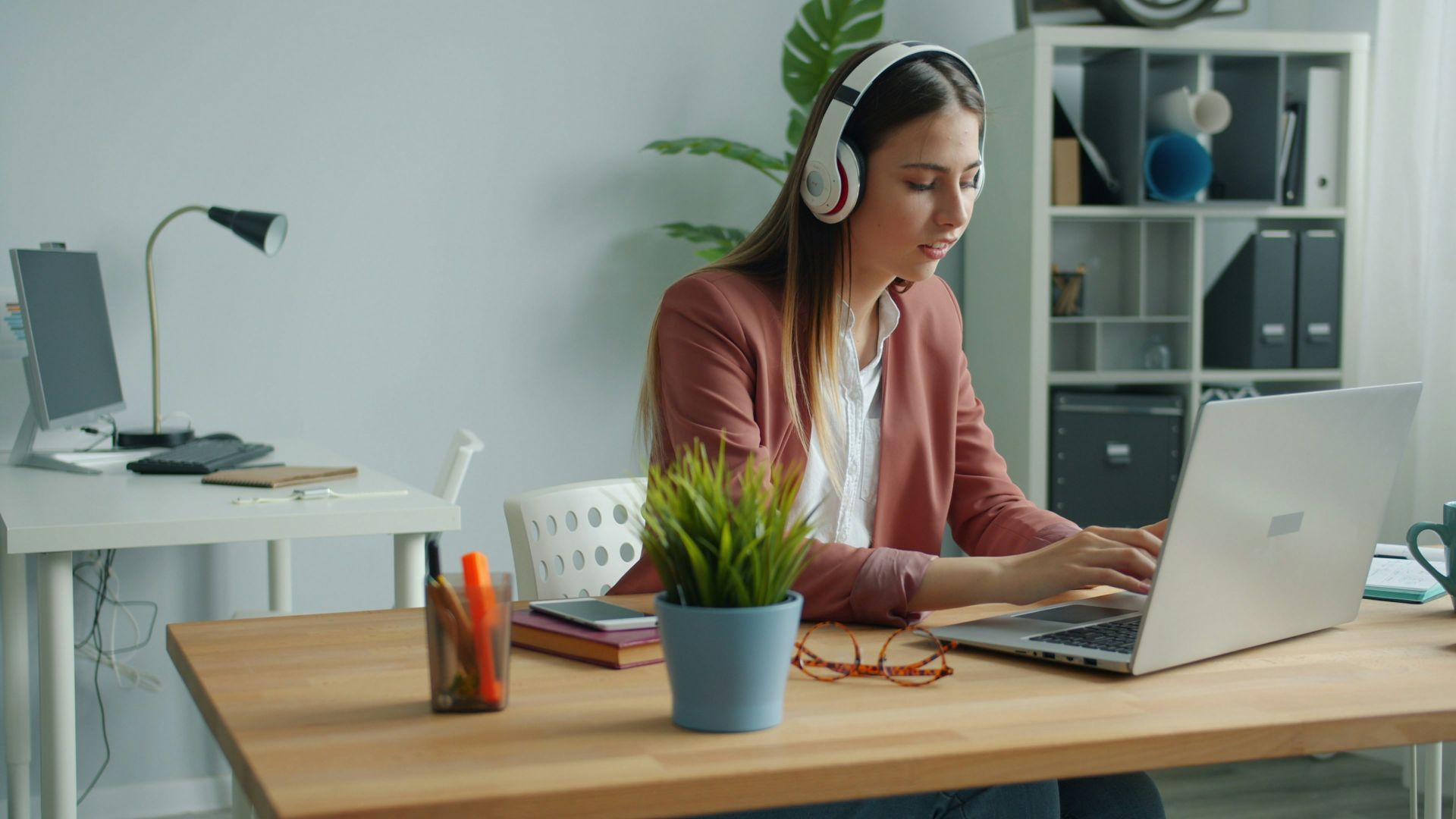 Woman wearing headphones working on laptop at desk.