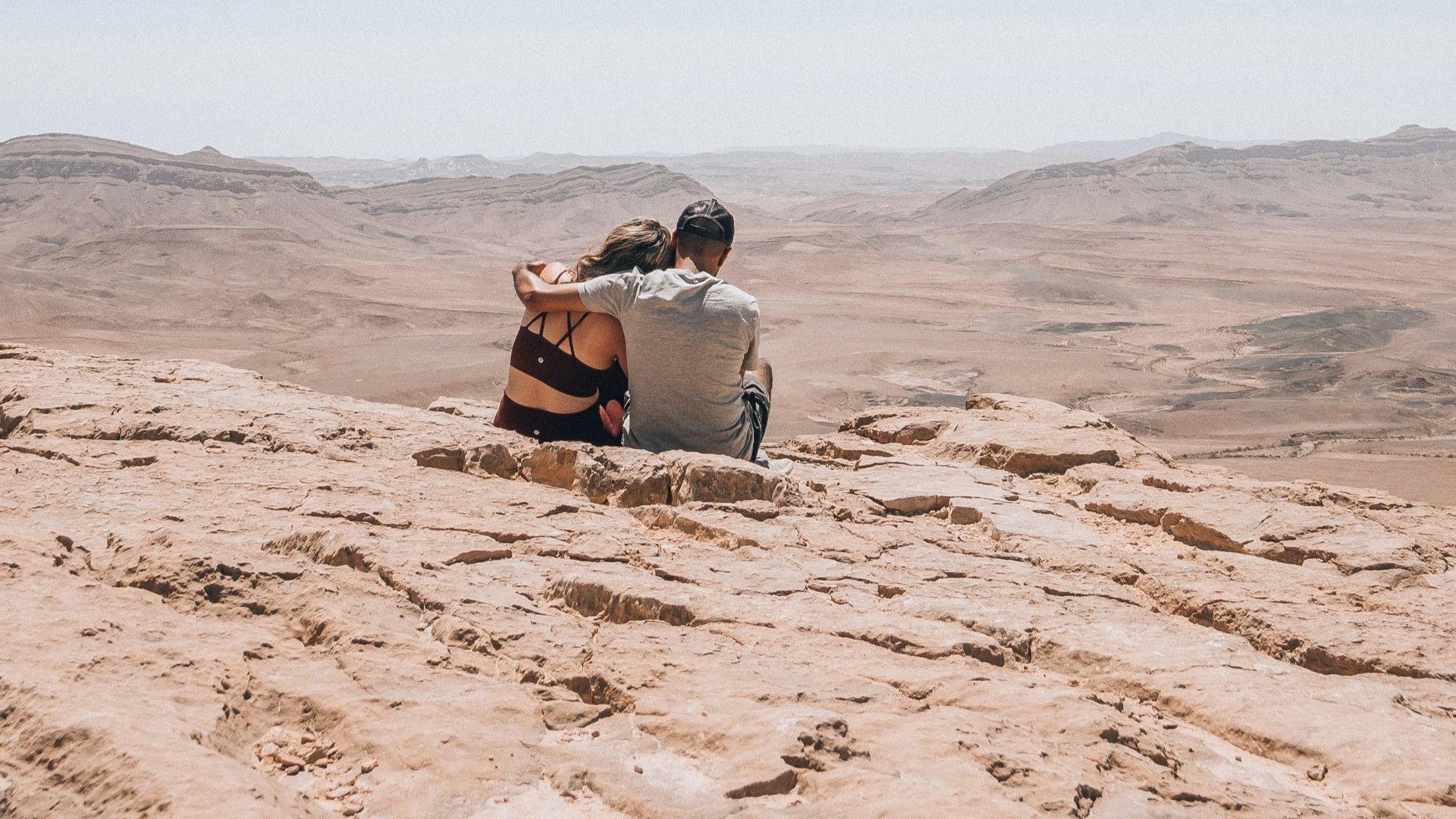 a man and woman sitting on a sandy hill