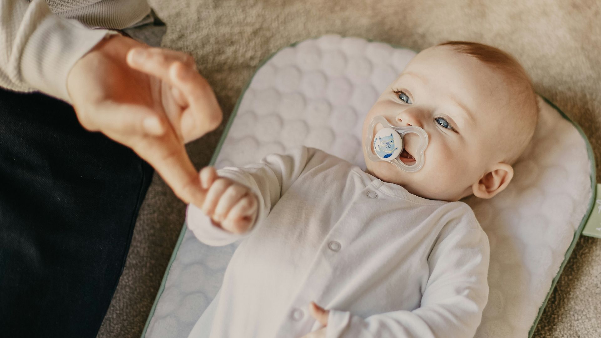 baby in white onesie lying on white textile