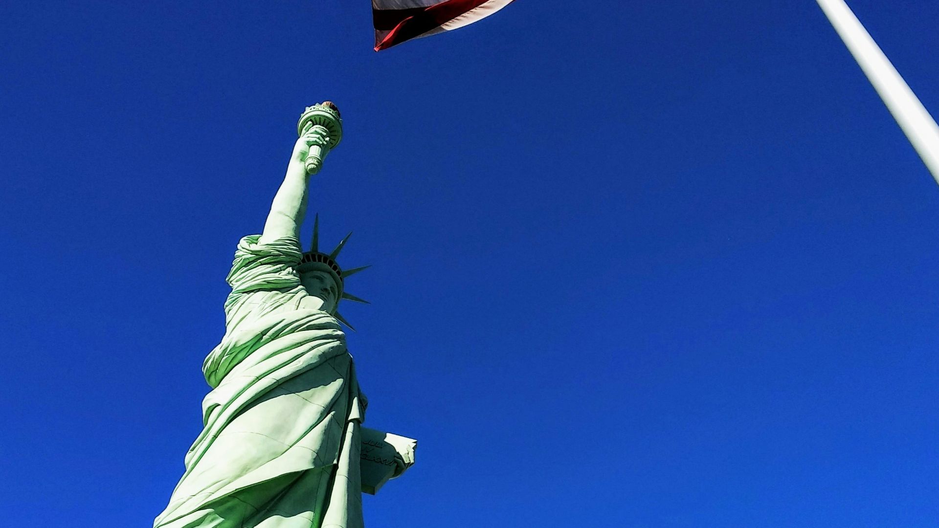 Statue of Liberty in front USA flag under blue sky