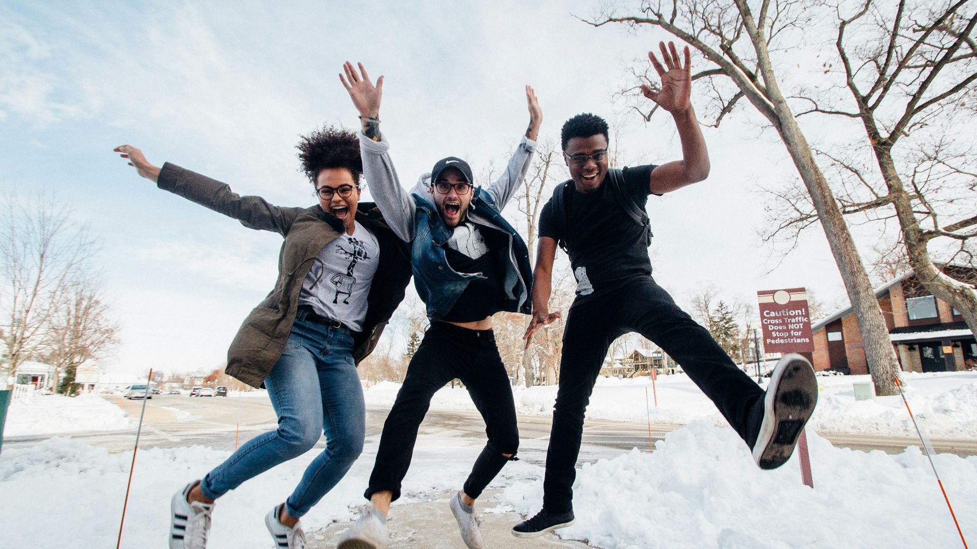 photo of three men jumping on ground near bare trees during daytime
