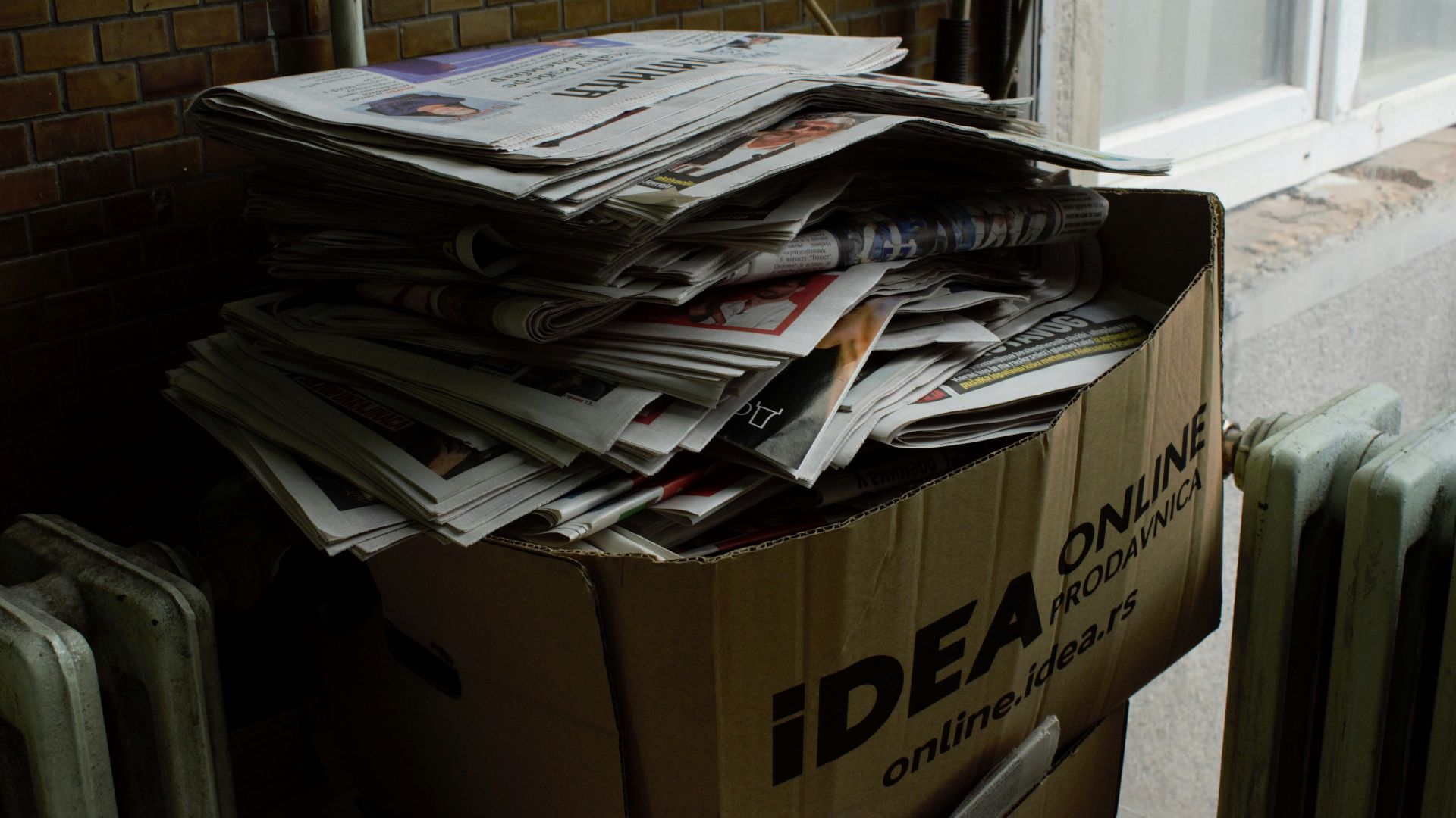 a cardboard box filled with newspapers next to a radiator