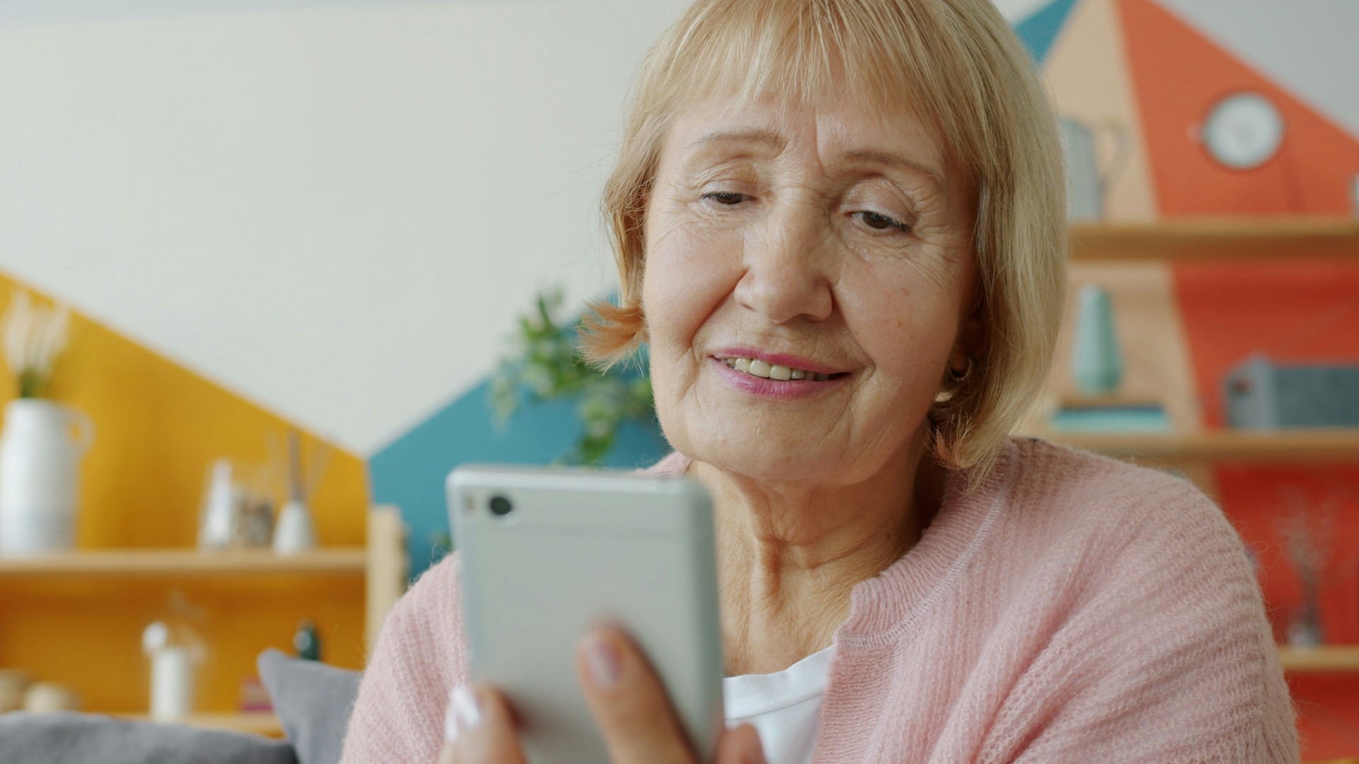 Elderly woman smiling while looking at smartphone.