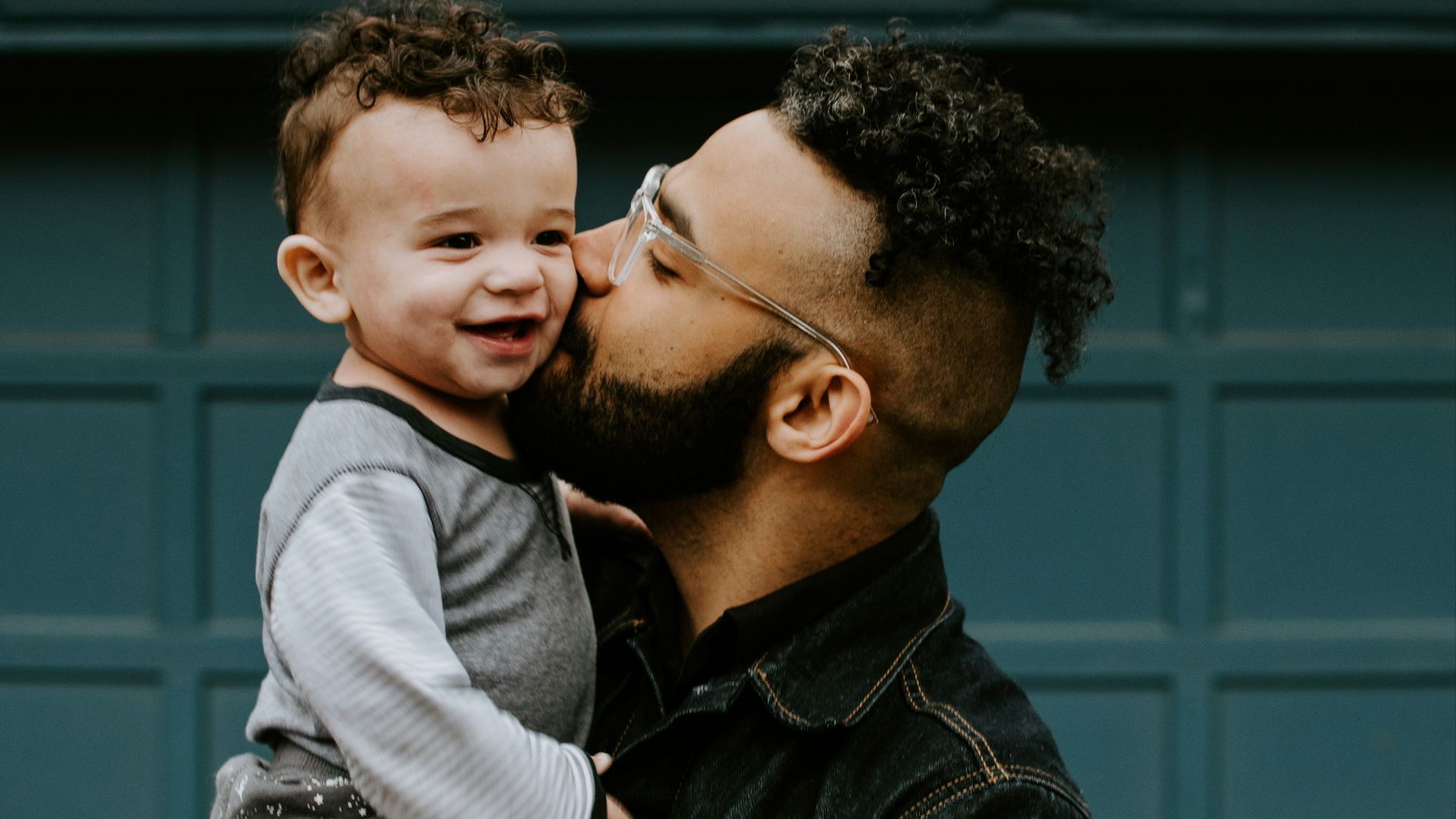 man carrying baby boy and kissing on cheek