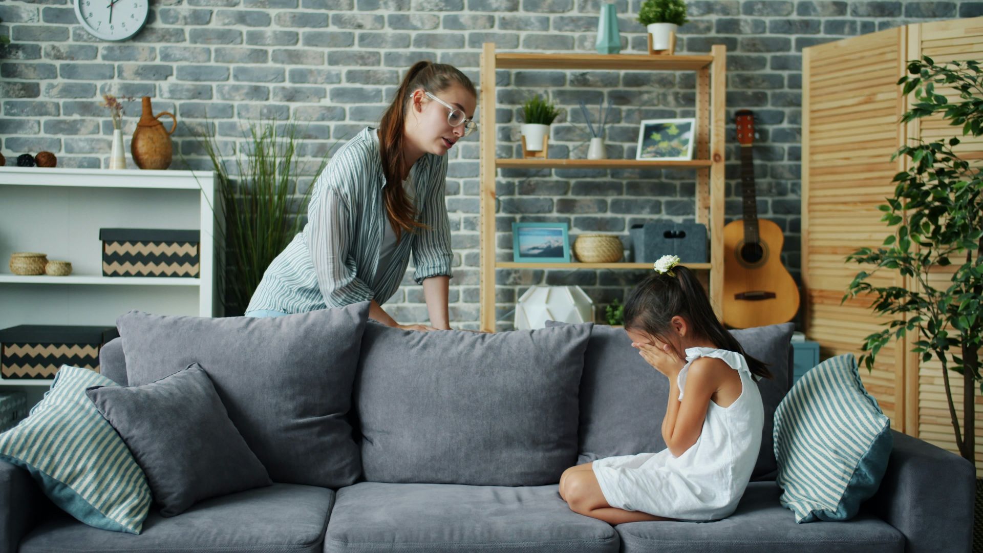 Mother scolds crying daughter on sofa in living room.