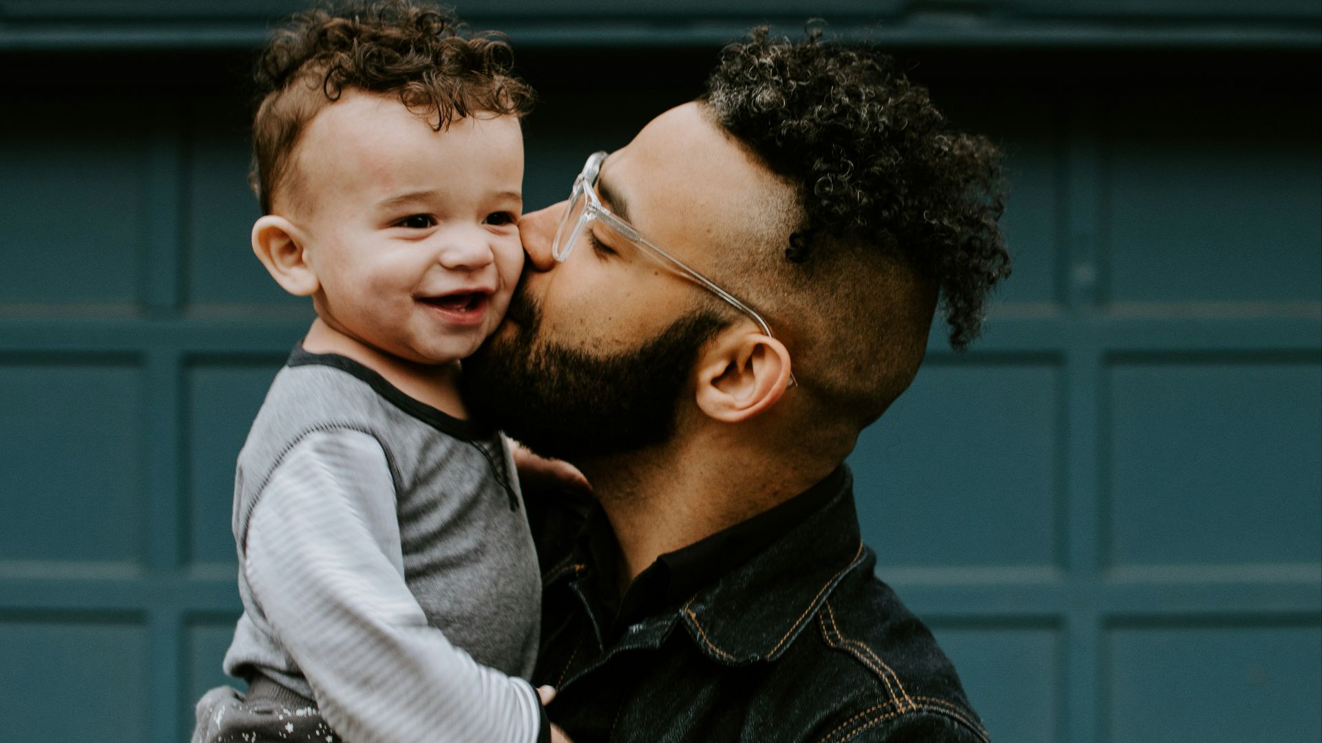 man carrying baby boy and kissing on cheek