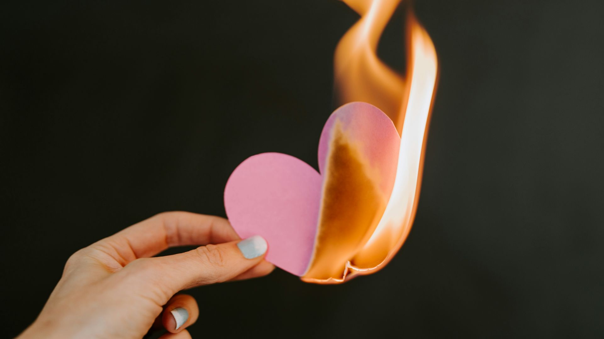 a person holding a paper heart in front of a fire
