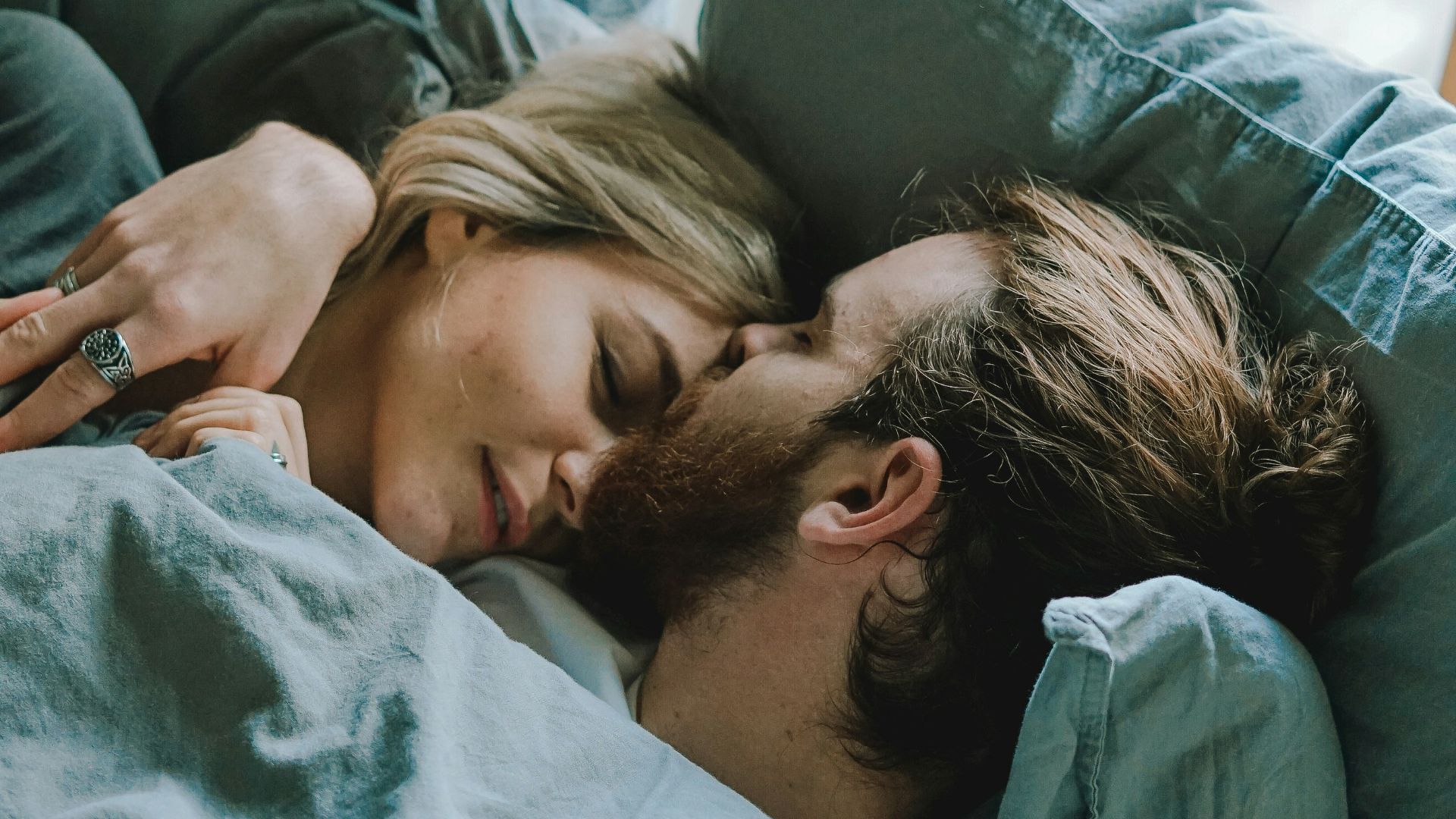 man kissing woman's forehead while lying on bed